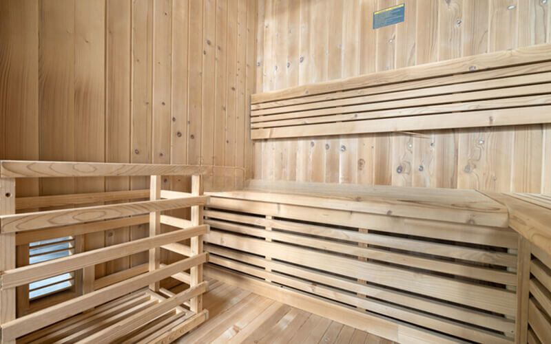 Wood-paneled sauna with wooden benches and slatted backrests in a warm, empty interior