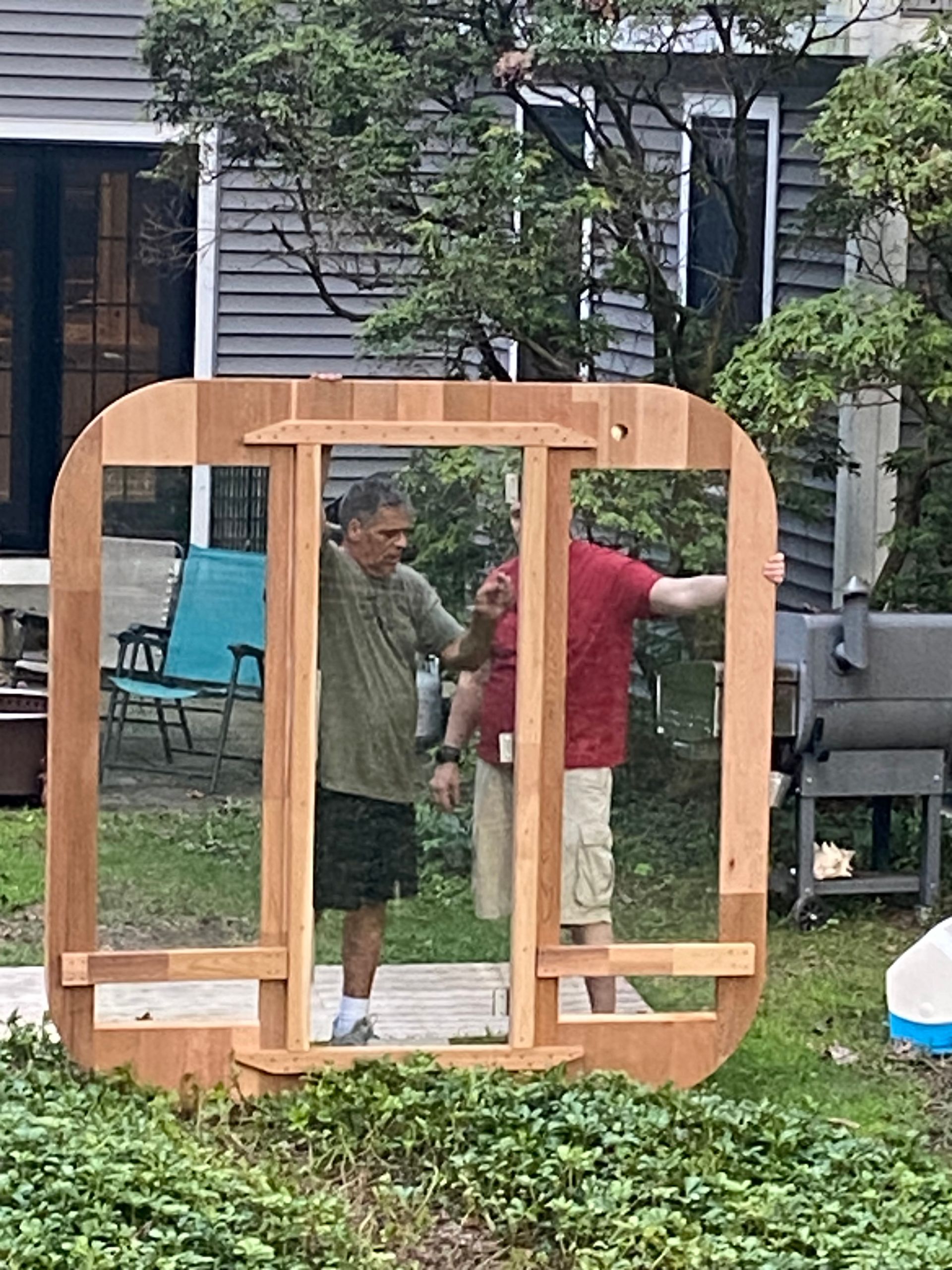 Two people assembling a wooden frame in a backyard, with a house and trees in the background.