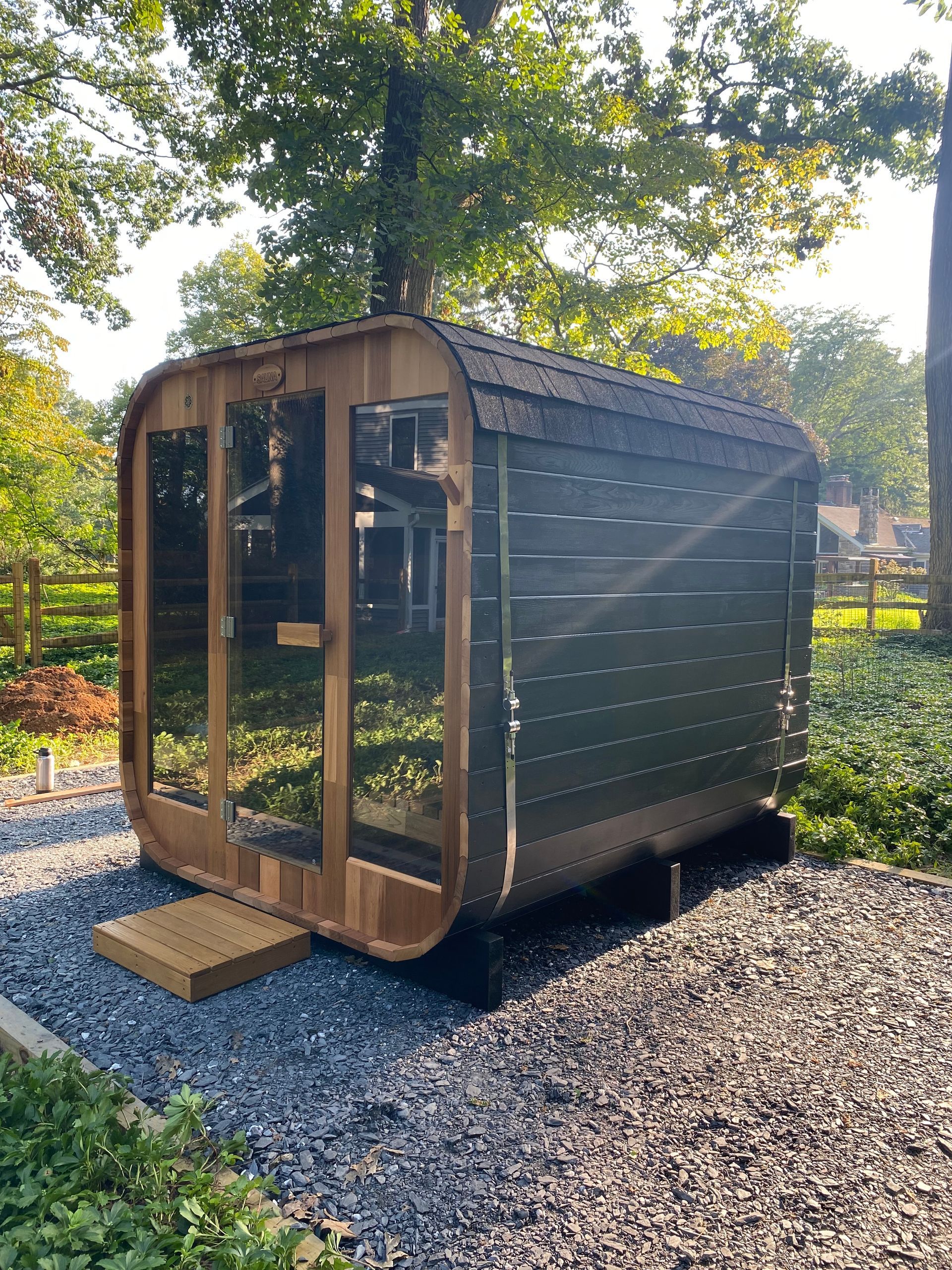Small wooden garden shed with glass doors on a gravel path under trees