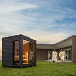 Modern outdoor patio with a black garden office pod and two white sculptures on a lawn at sunset