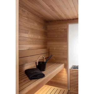 Wood-paneled sauna bench with a black towel and bucket, beside a glass door