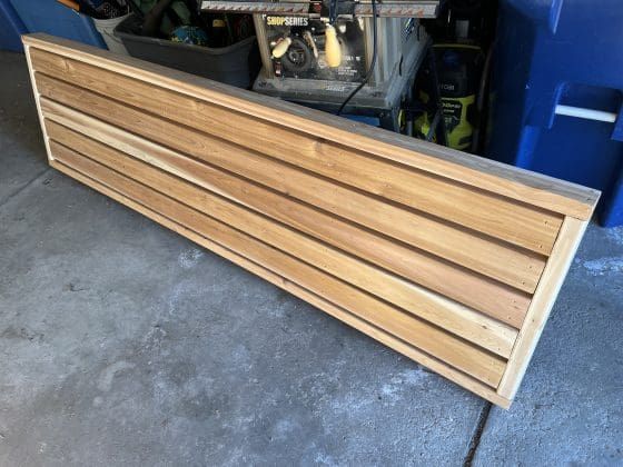 Long wooden slatted panel leaning in a garage, with a metal frame and car in the background
