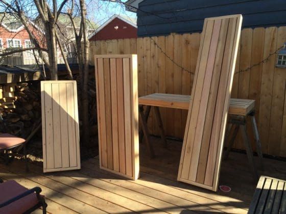 Three wooden panel doors leaning on a sunlit deck near a fence and table saws