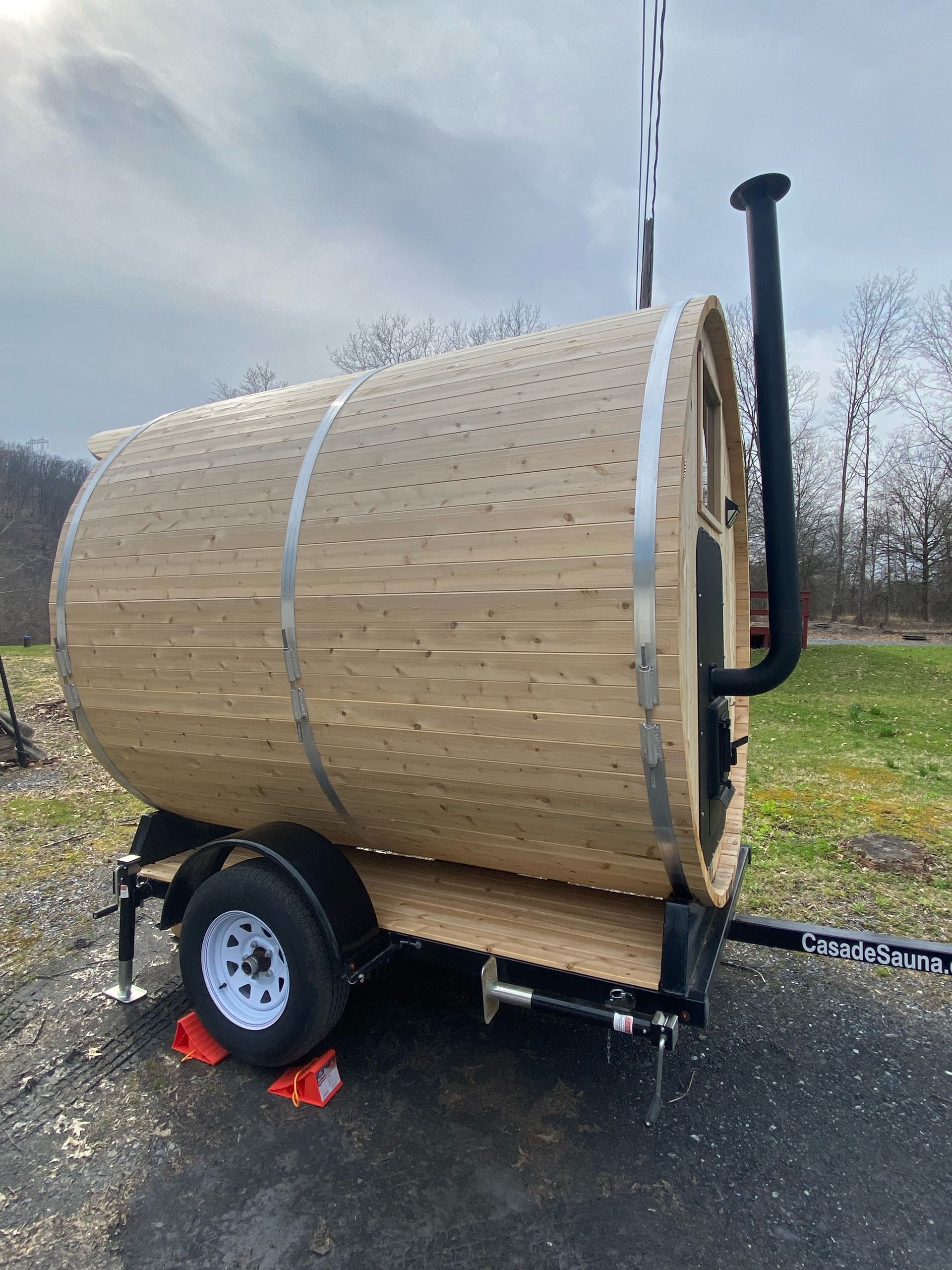 Wood-fired barrel-shaped trailer smoker with black chimney, parked on gravel outdoors.