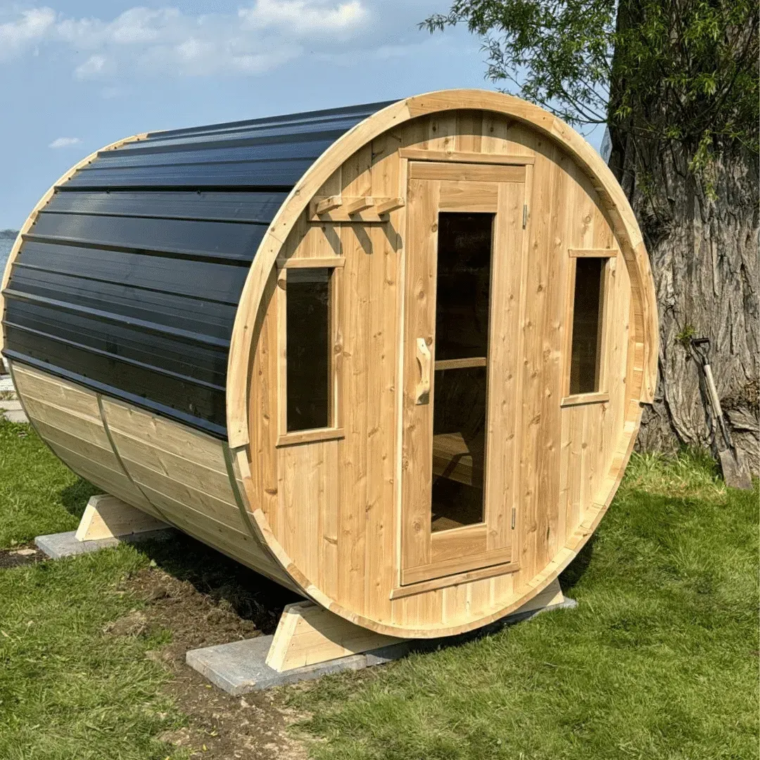 Wooden 6 person barrel-shaped outdoor sauna with black curved siding, set on grass beside a tree.