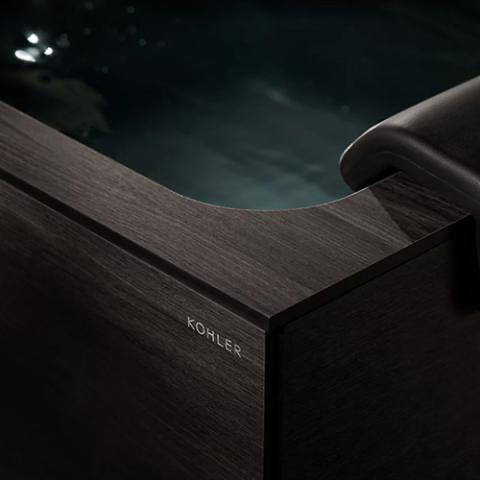 Close-up of a dark wood-grain Kohler sink or tub edge with a sleek black fixture handle