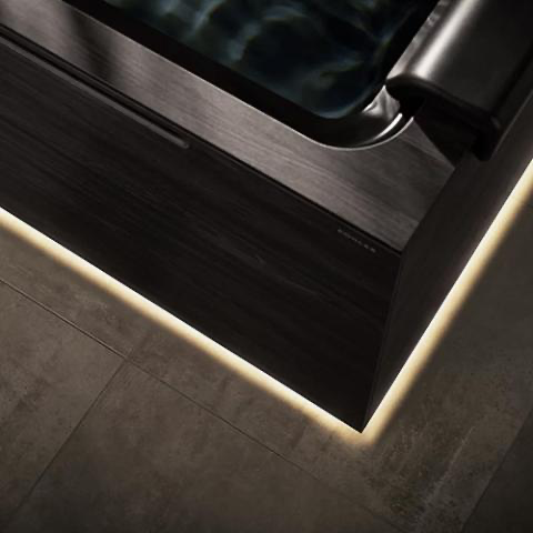 Close-up of a brushed metal appliance corner with black paneling and warm underlighting on tiled floor