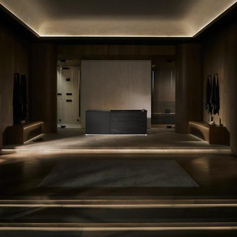 Dim modern hotel lobby with dark wood walls, central reception desk, and warm ceiling lighting