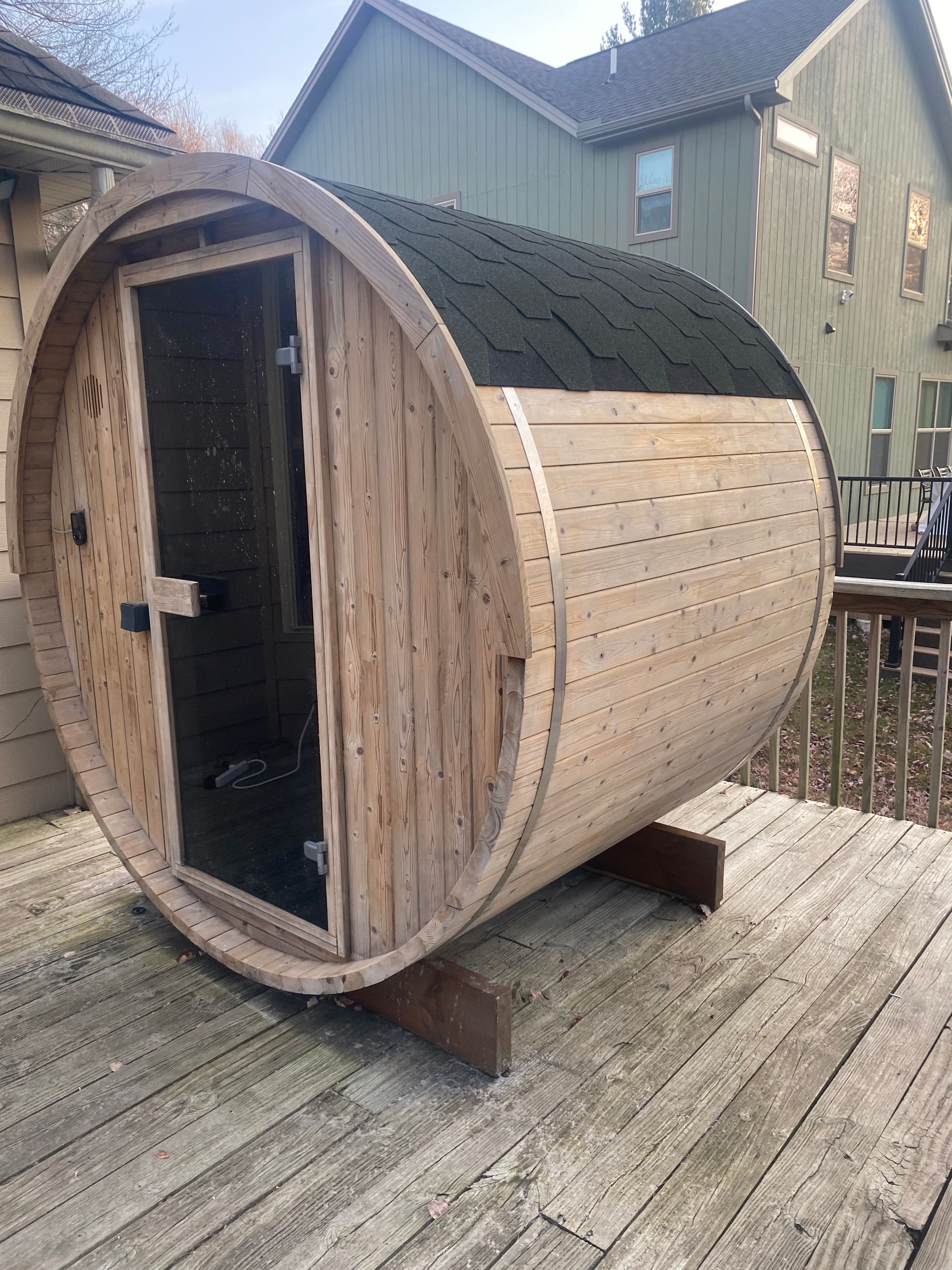 Wooden barrel sauna with open front door on a deck outdoors