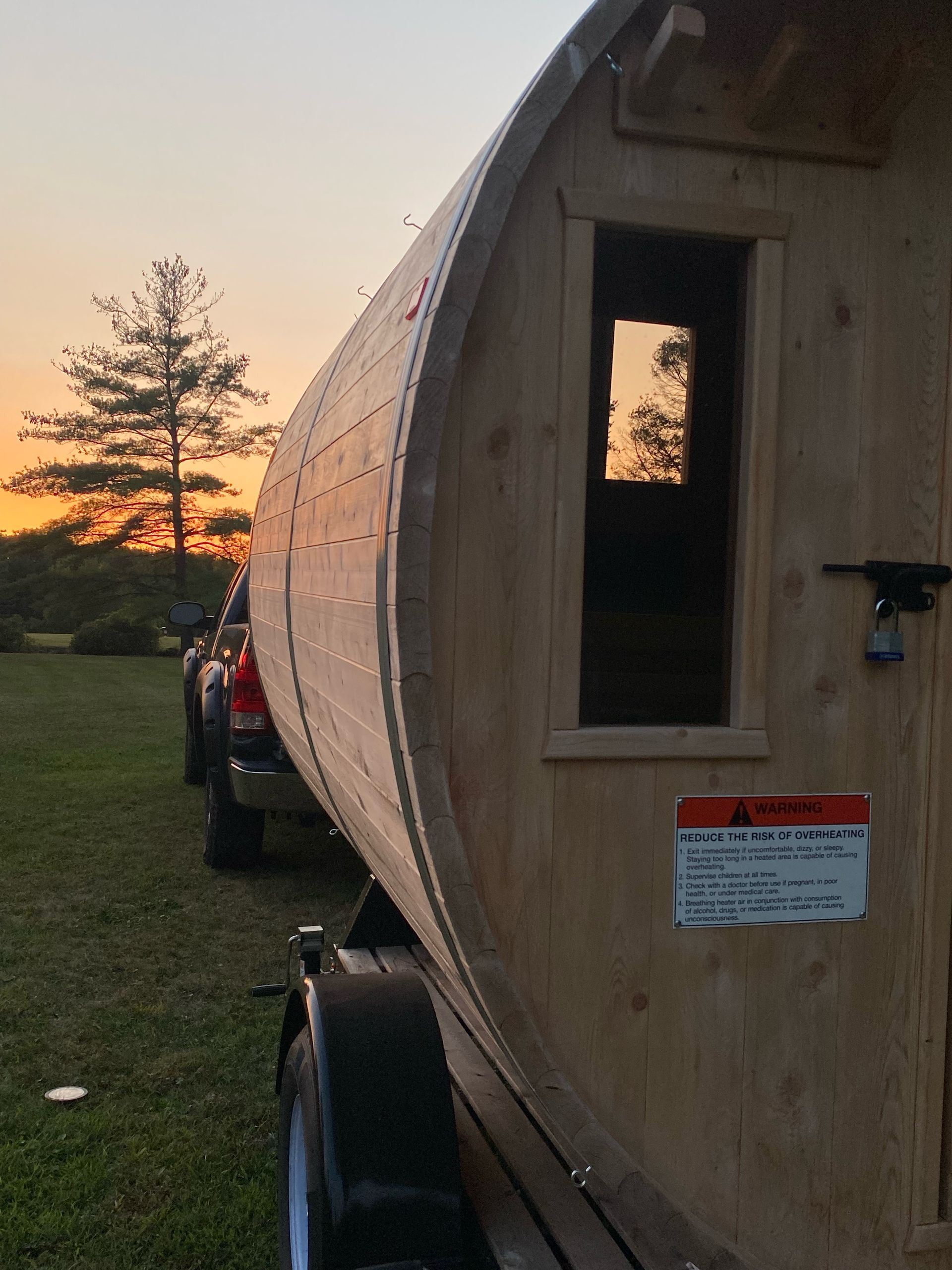 Wooden teardrop camper at sunset on a grassy field with a small window and trailer wheel visible