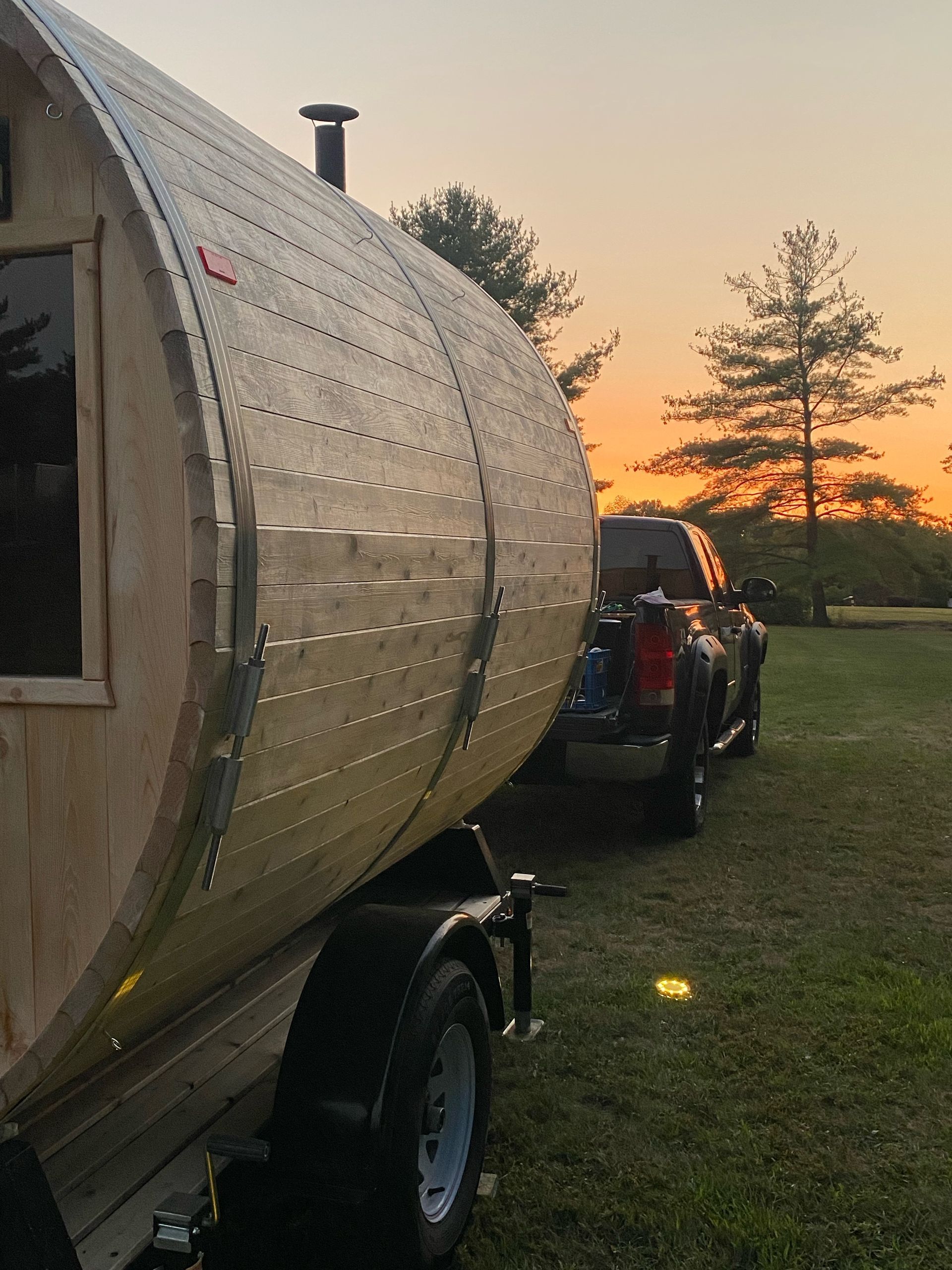 A silver trailer caravan hitched to a black vehicle on a grassy field at sunset