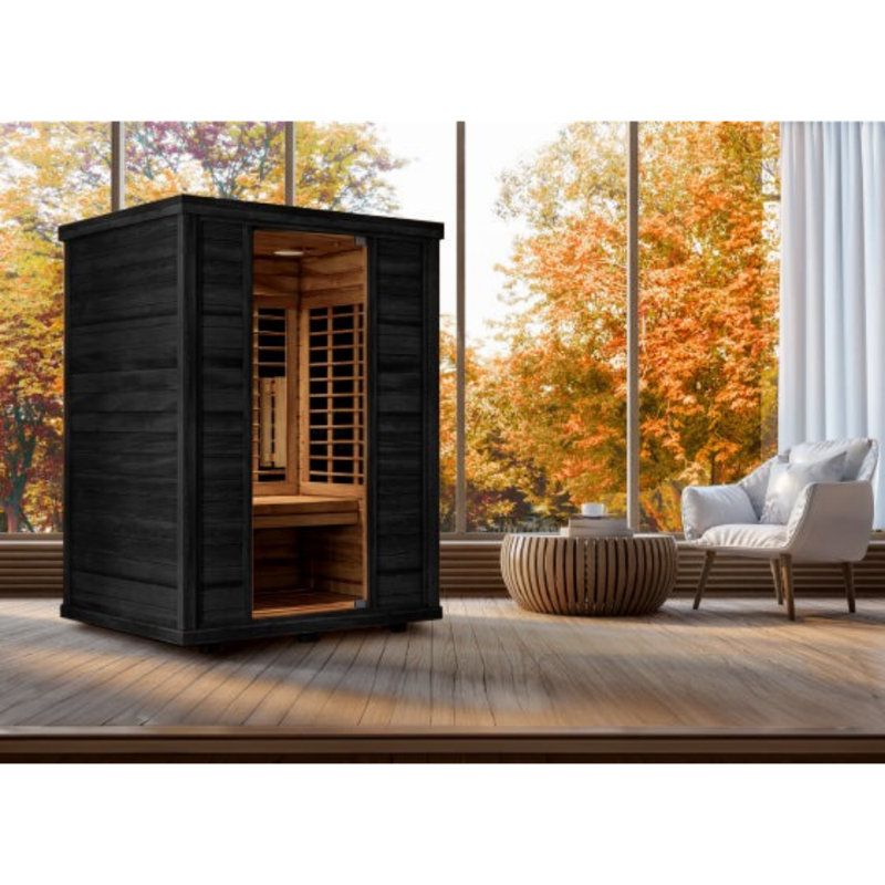 Black outdoor sauna on a wooden deck beside lounge chairs, with autumn trees beyond the glass wall.
