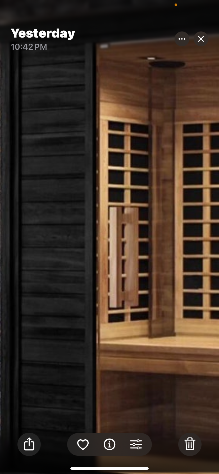 Wooden sauna interior with benches, lattice screens, and a dark sliding door under warm lighting, outdoor infrared sauna