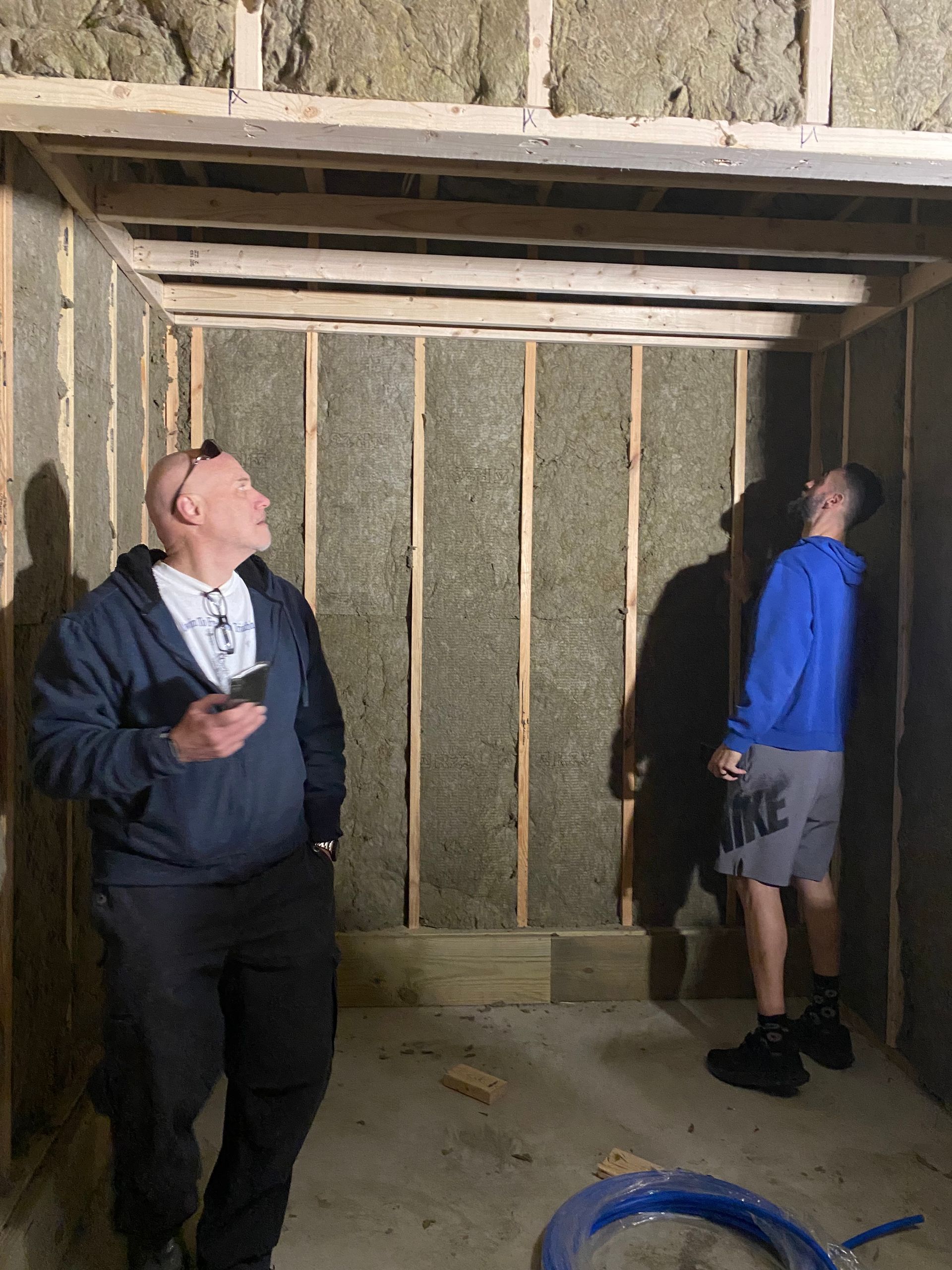 Two people in a wooden shed-like room, both looking up at the ceiling beams.