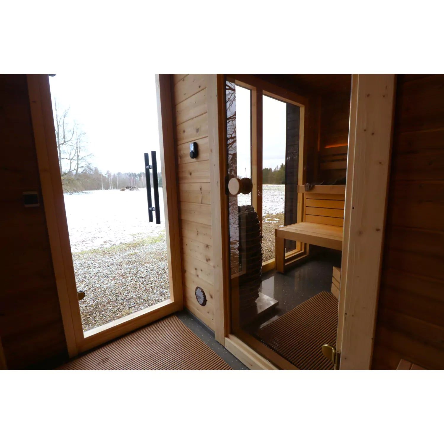 Wooden sauna interior with open glass door looking out to a snowy landscape