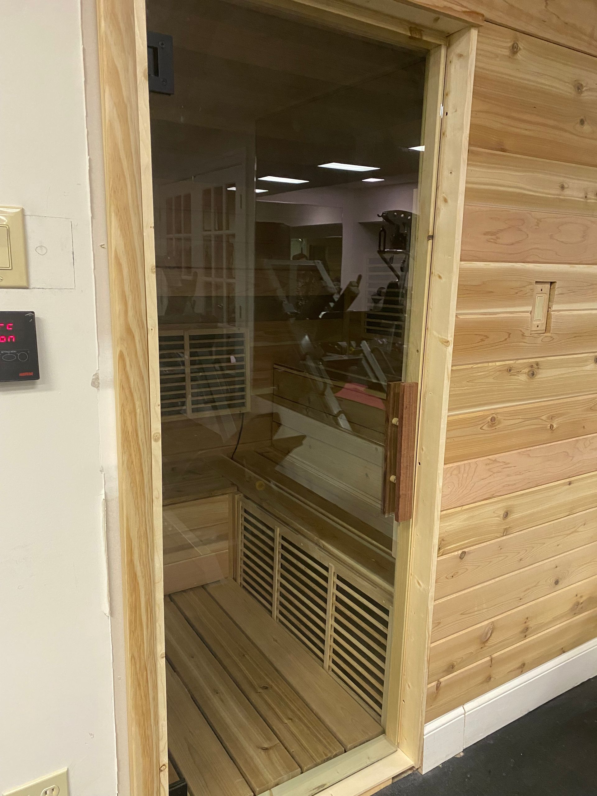 Open sauna doorway with wood-paneled walls and a control panel on the left.