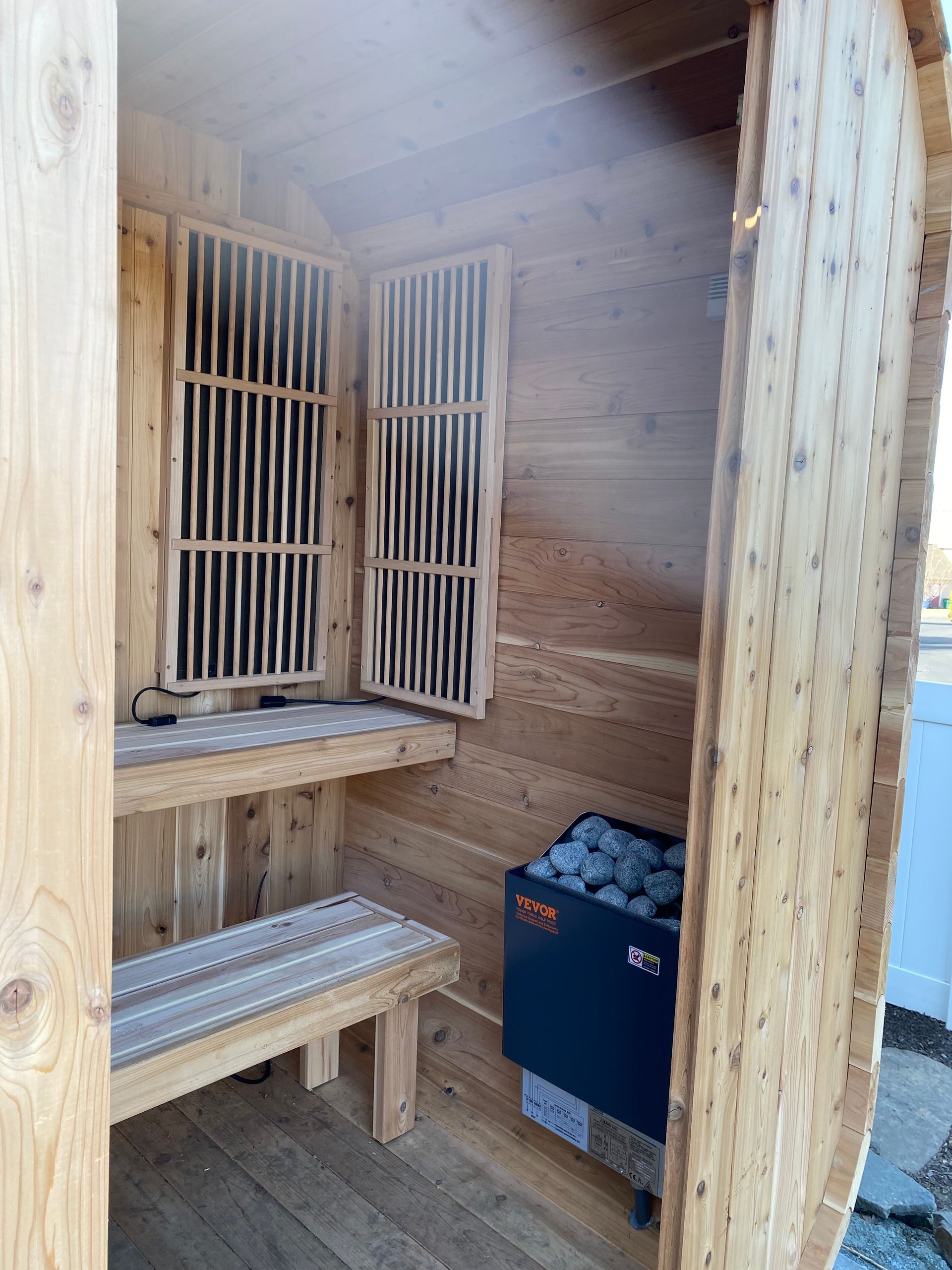 Wooden sauna interior with benches, louvered vents, and a small heater on the floor.