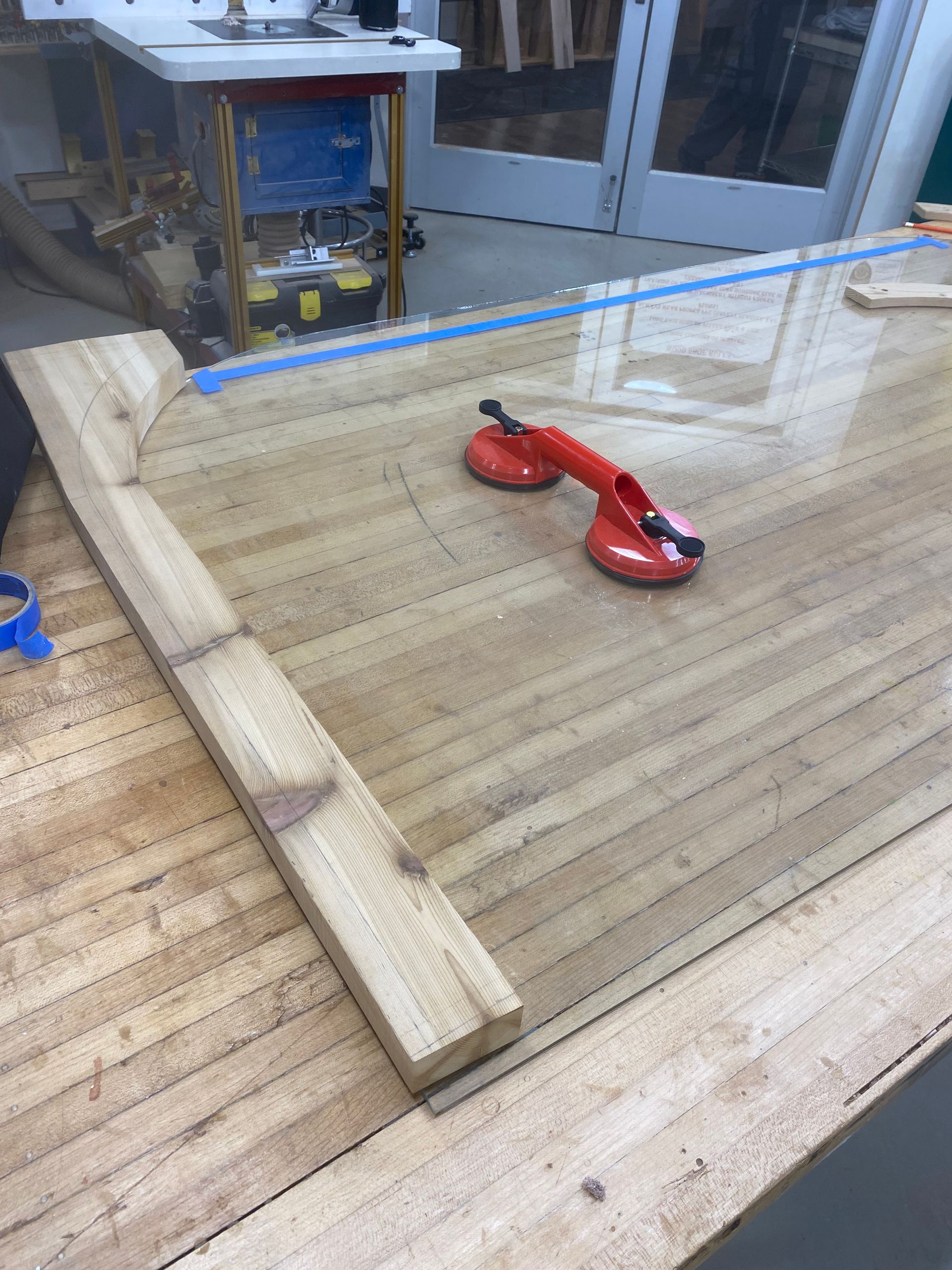 Red hand plane on a wooden workbench with lumber and a cabinet saw in the background.