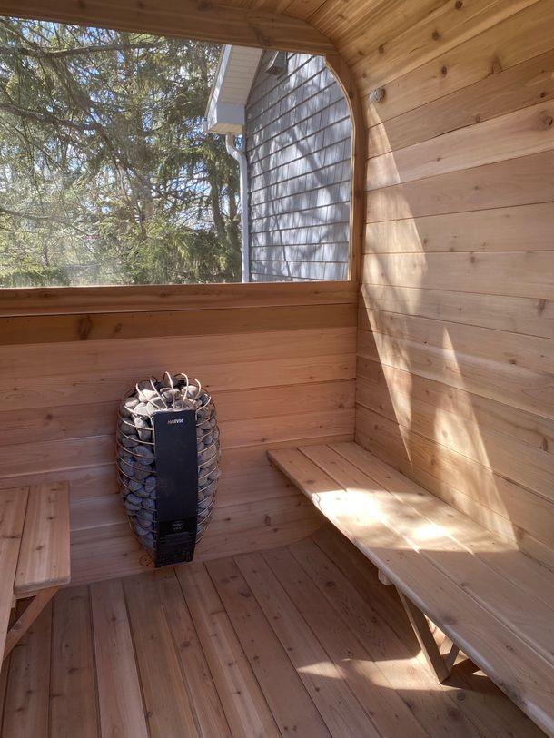 Wooden sauna interior with bench seating, a heater, and a large arched window overlooking trees