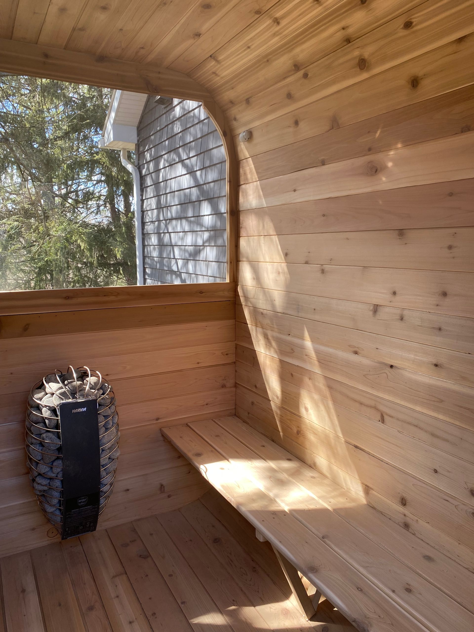 Wooden sauna interior with a stone heater and a small window overlooking trees