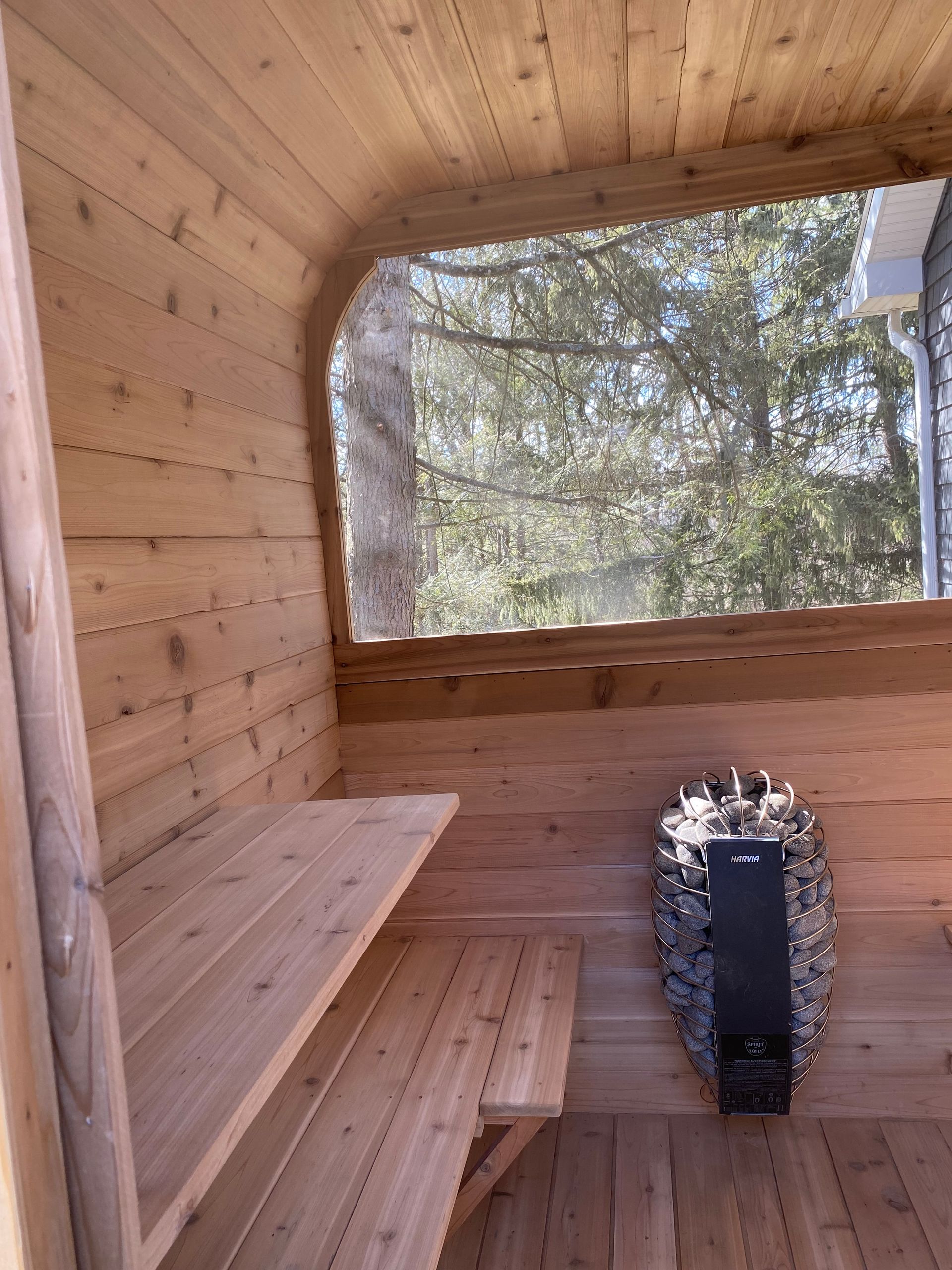 Wooden sauna interior with benches, a window, and a glowing stove heater