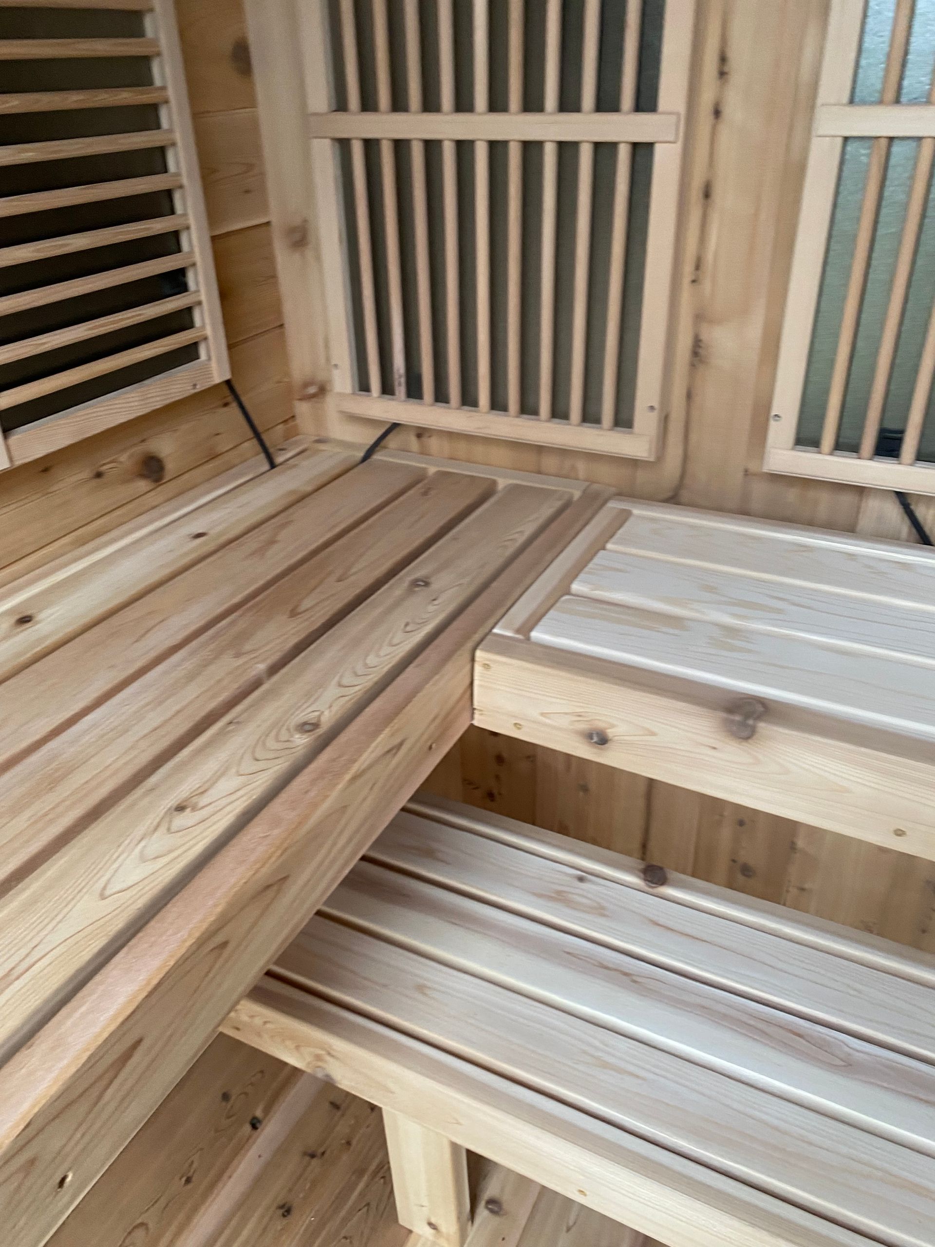 Wooden sauna interior with slatted benches and ventilation grilles around a corner seat.