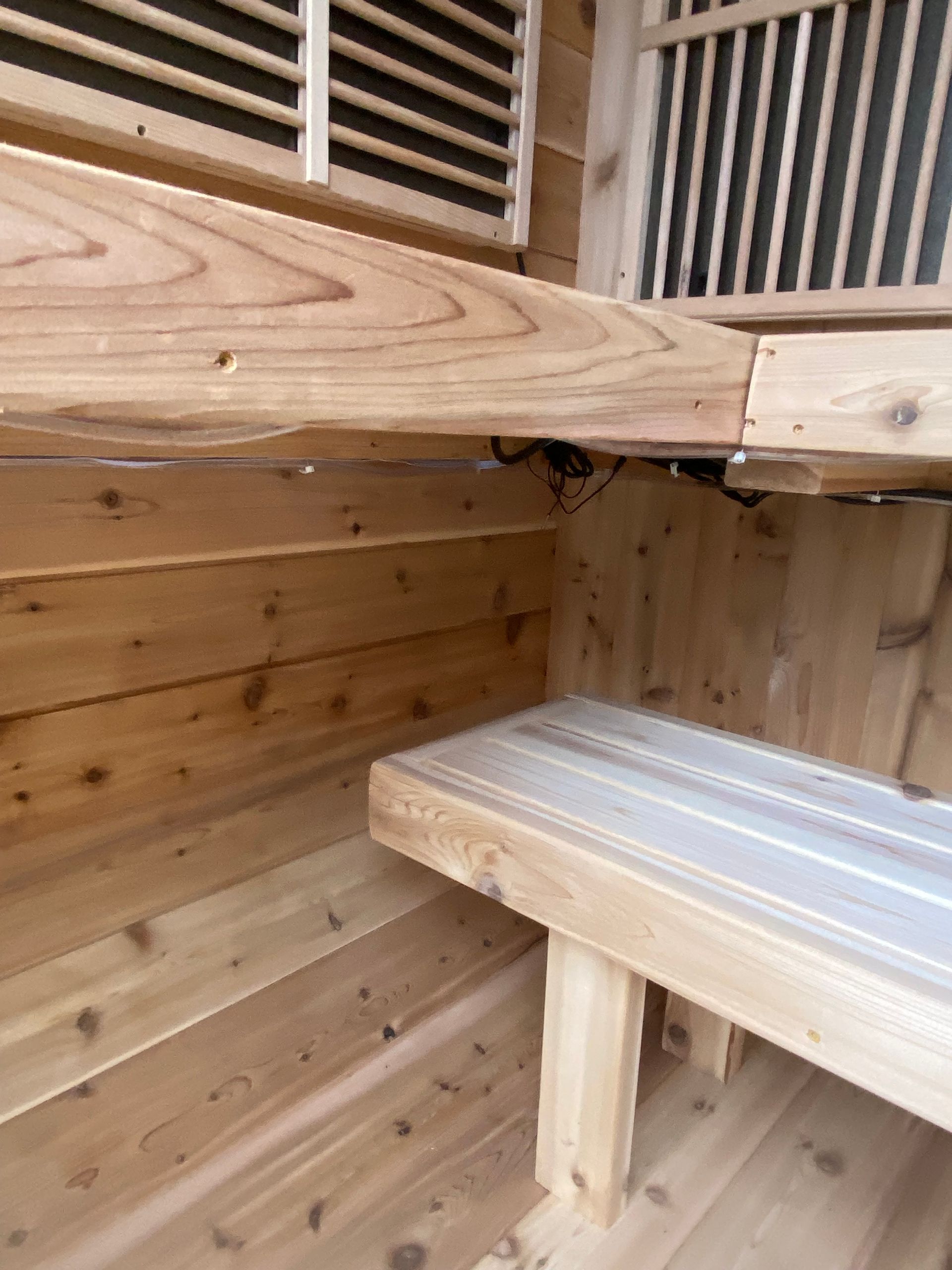 Wooden interior with bench and slatted wall, showing a small enclosed sauna-like space.