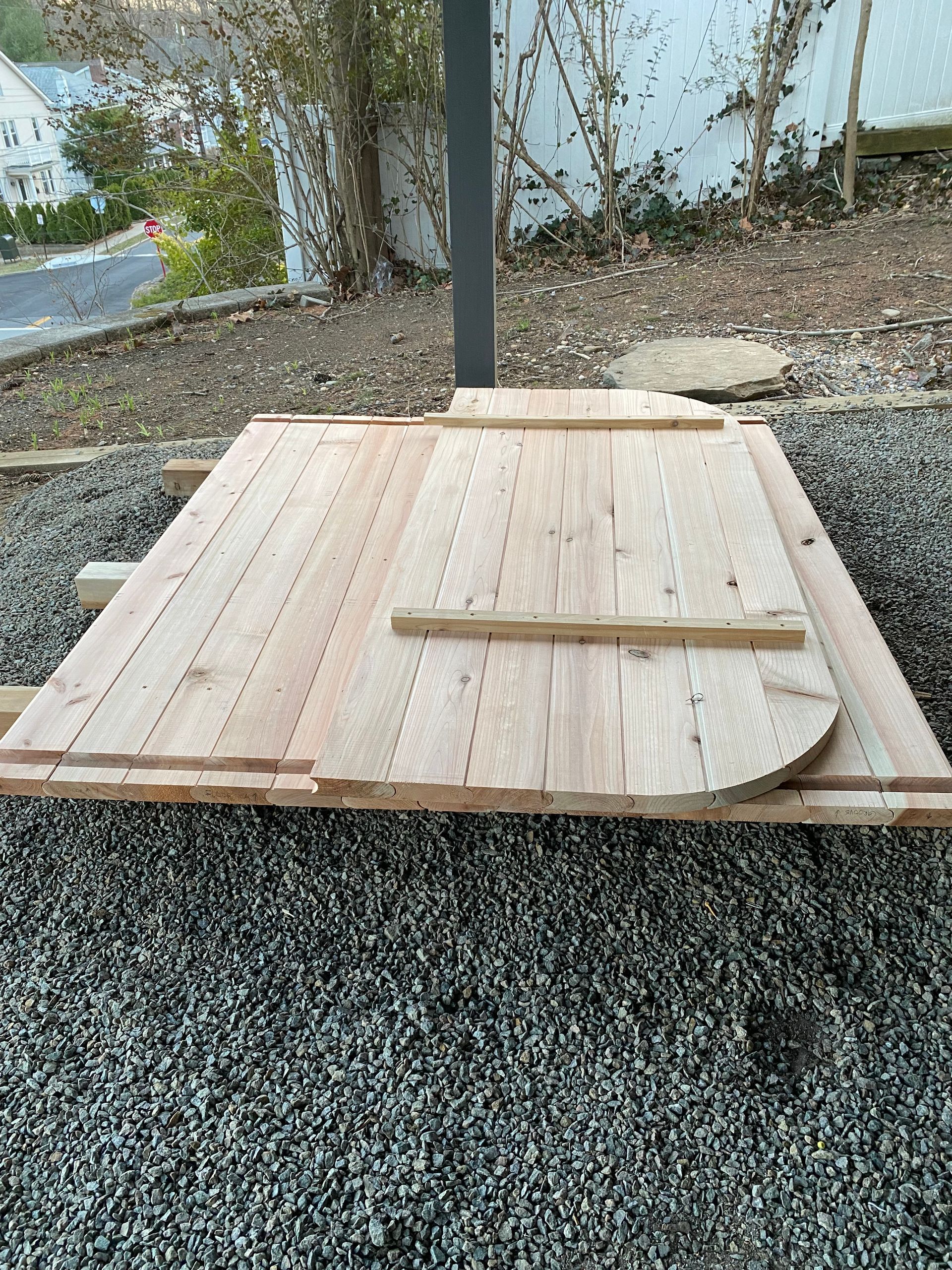 Plywood boards laid over gravel outdoors, forming a small platform or makeshift surface.