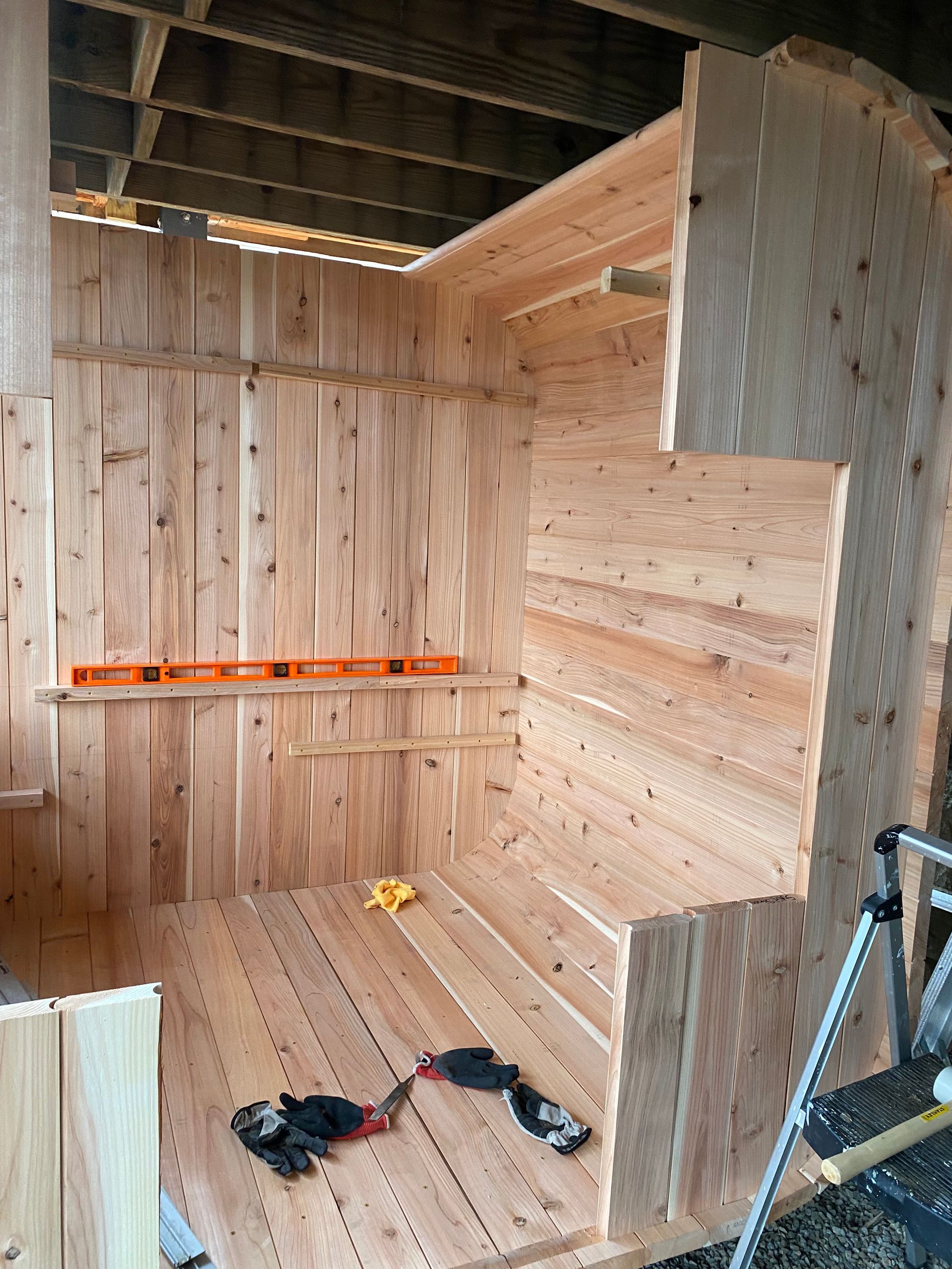 Wooden shed interior under construction with partially finished walls, floor planks, and tools on the floor