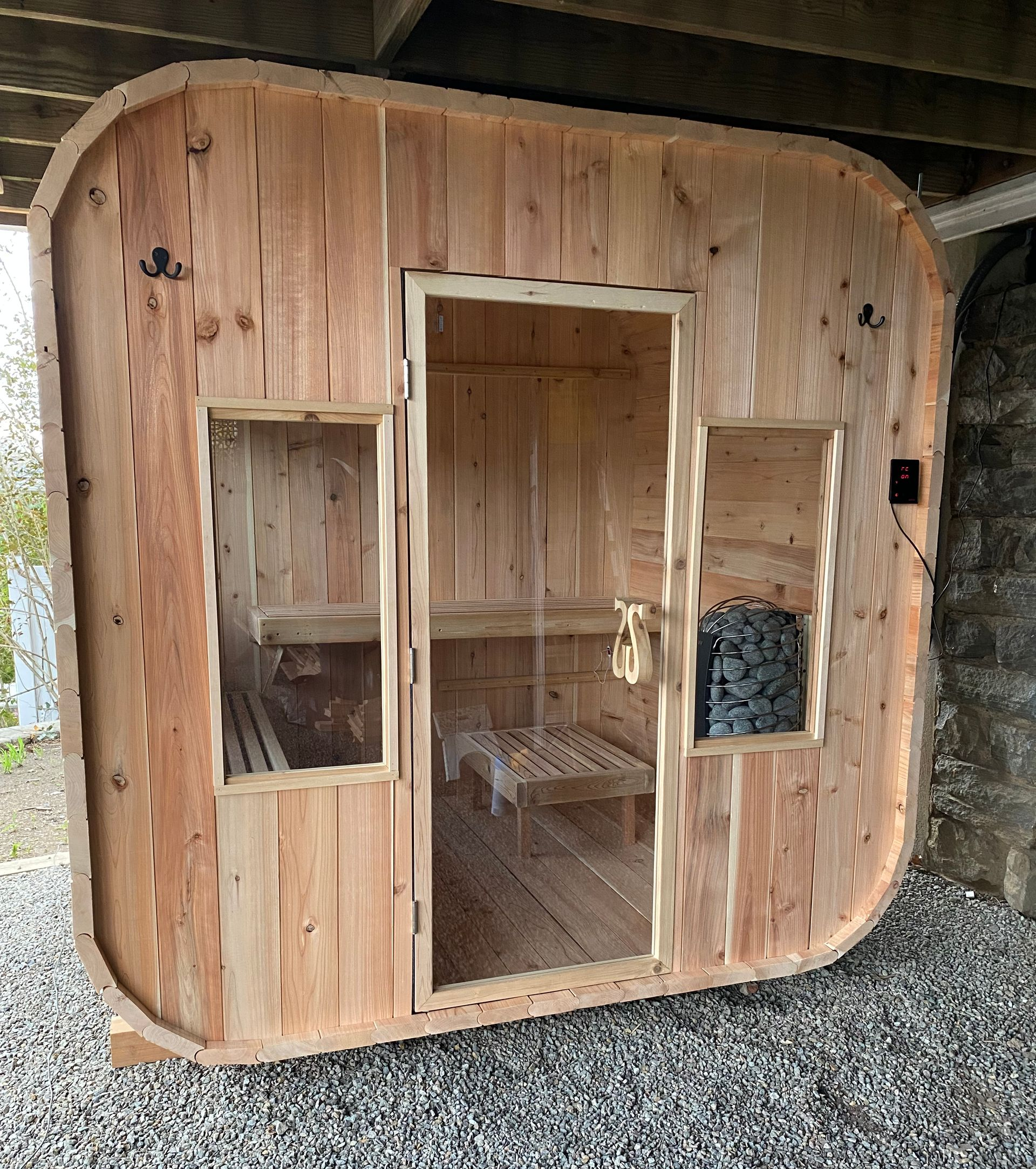 Wooden tiny cabin with a central door and two windows, set on gravel under a covered area