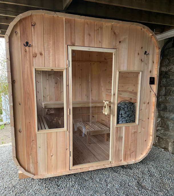 Wooden tiny cabin with a central door and two windows, set on gravel under a covered area
