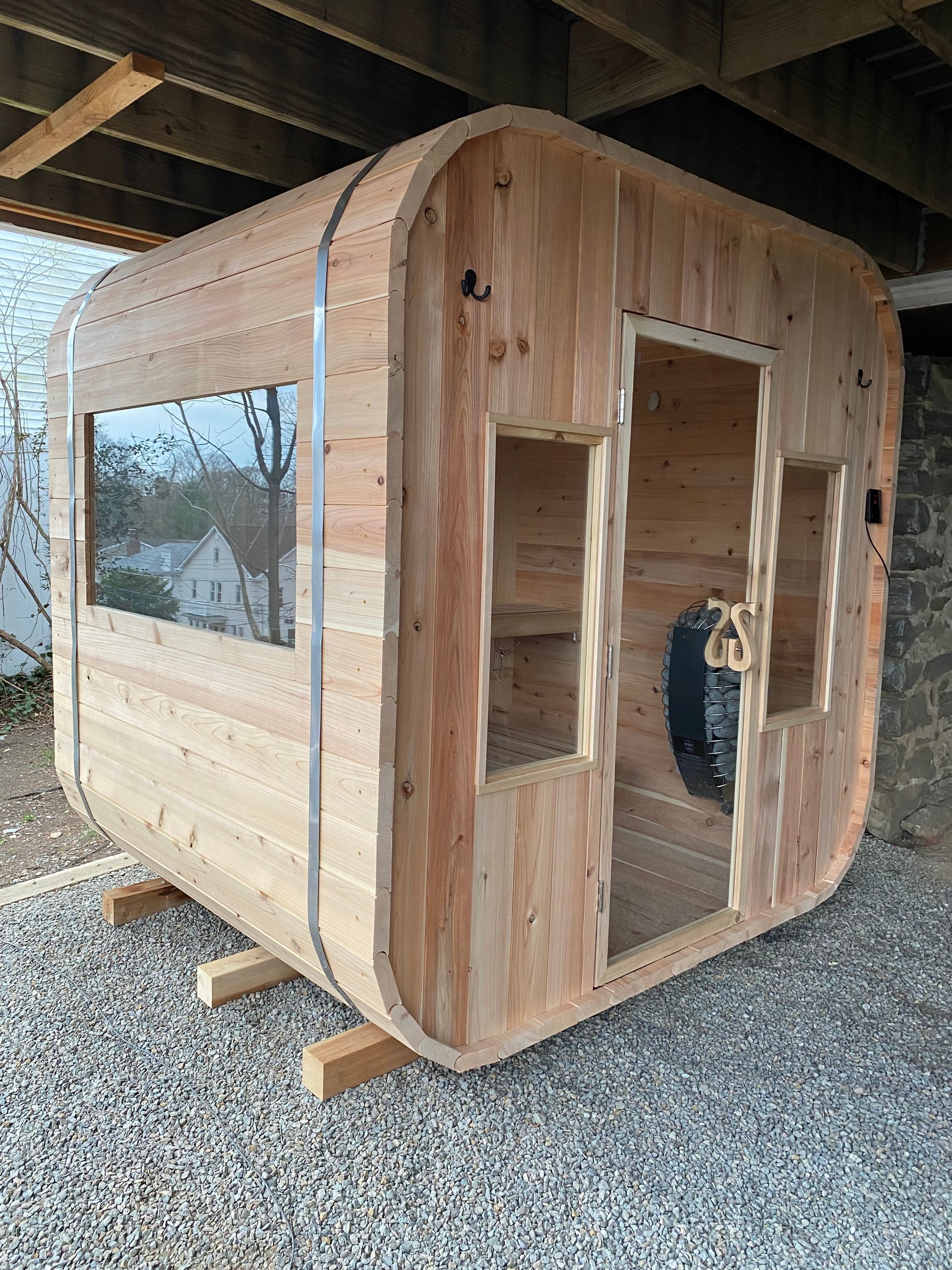 Wooden sauna pod under construction on gravel, with rounded front and side window.