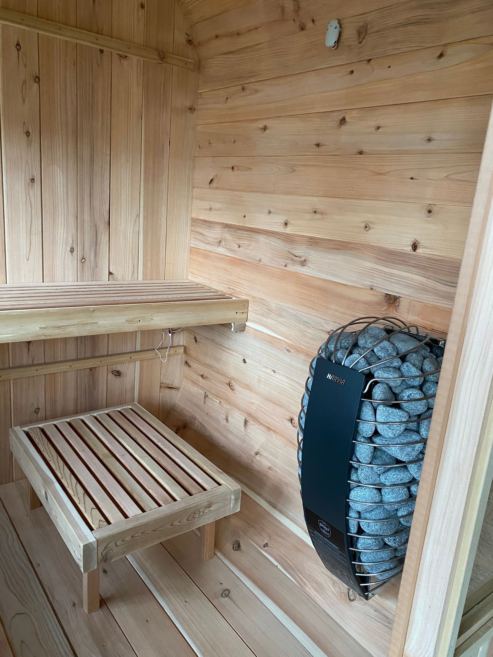 Wooden sauna interior with benches and a black stone heater against the wall