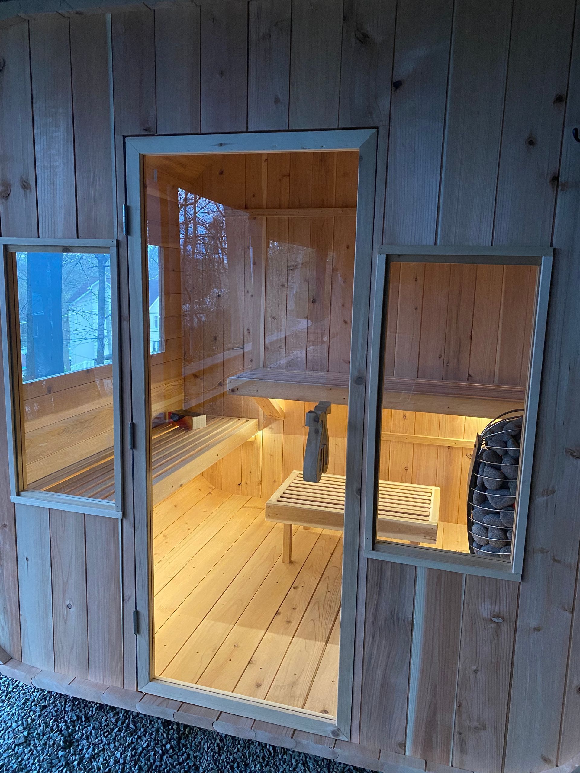 Wooden sauna interior viewed through an open door and side window, with warm lighting and benches.