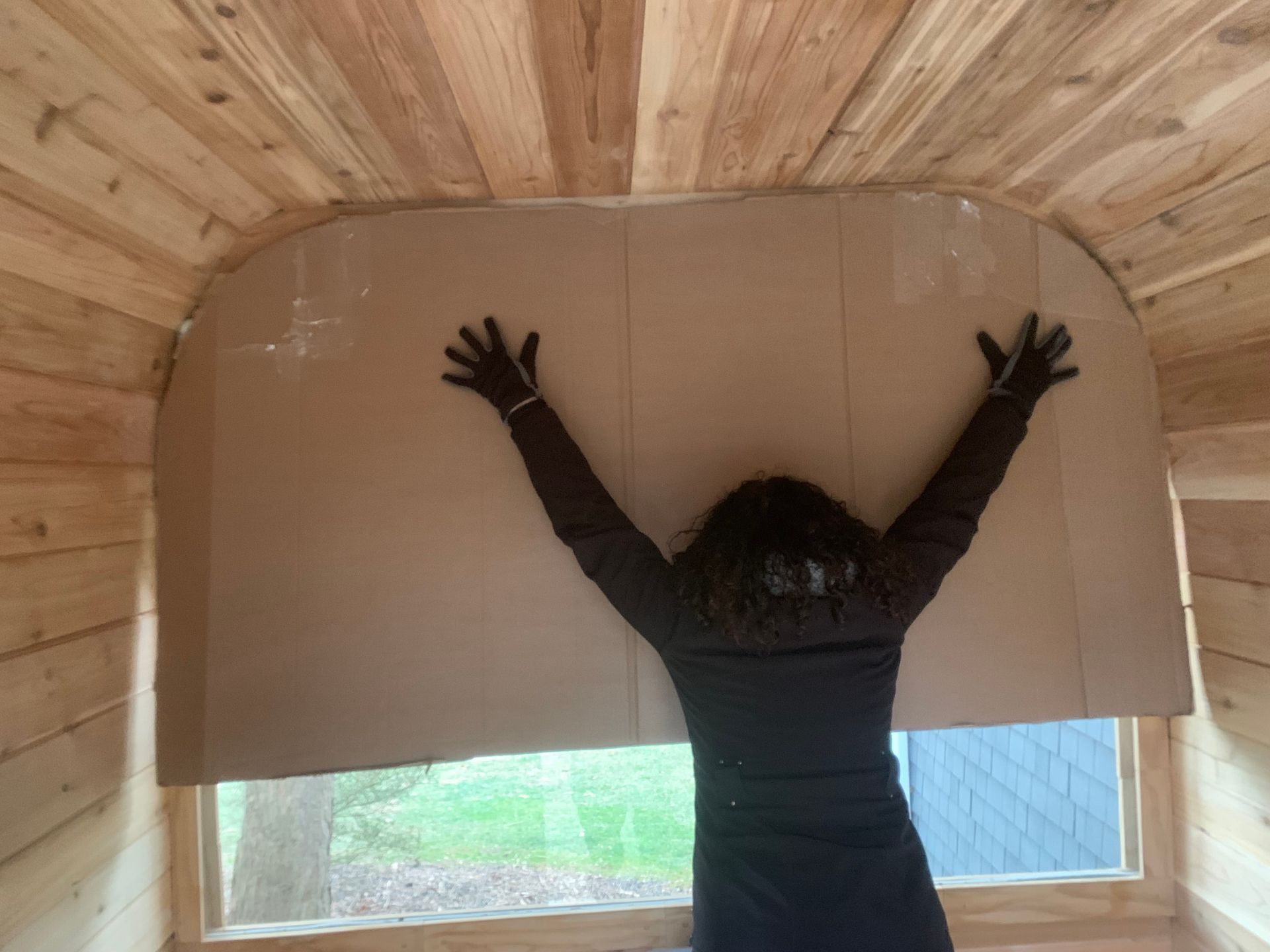 Person reaching up to adjust a large cardboard panel under a wooden arched ceiling.