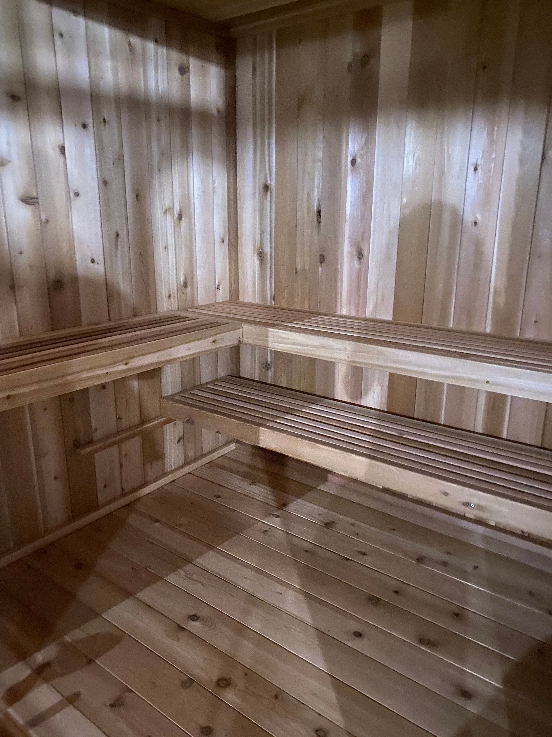 Wood-paneled sauna interior with wooden benches and slatted floor, lit by soft light.