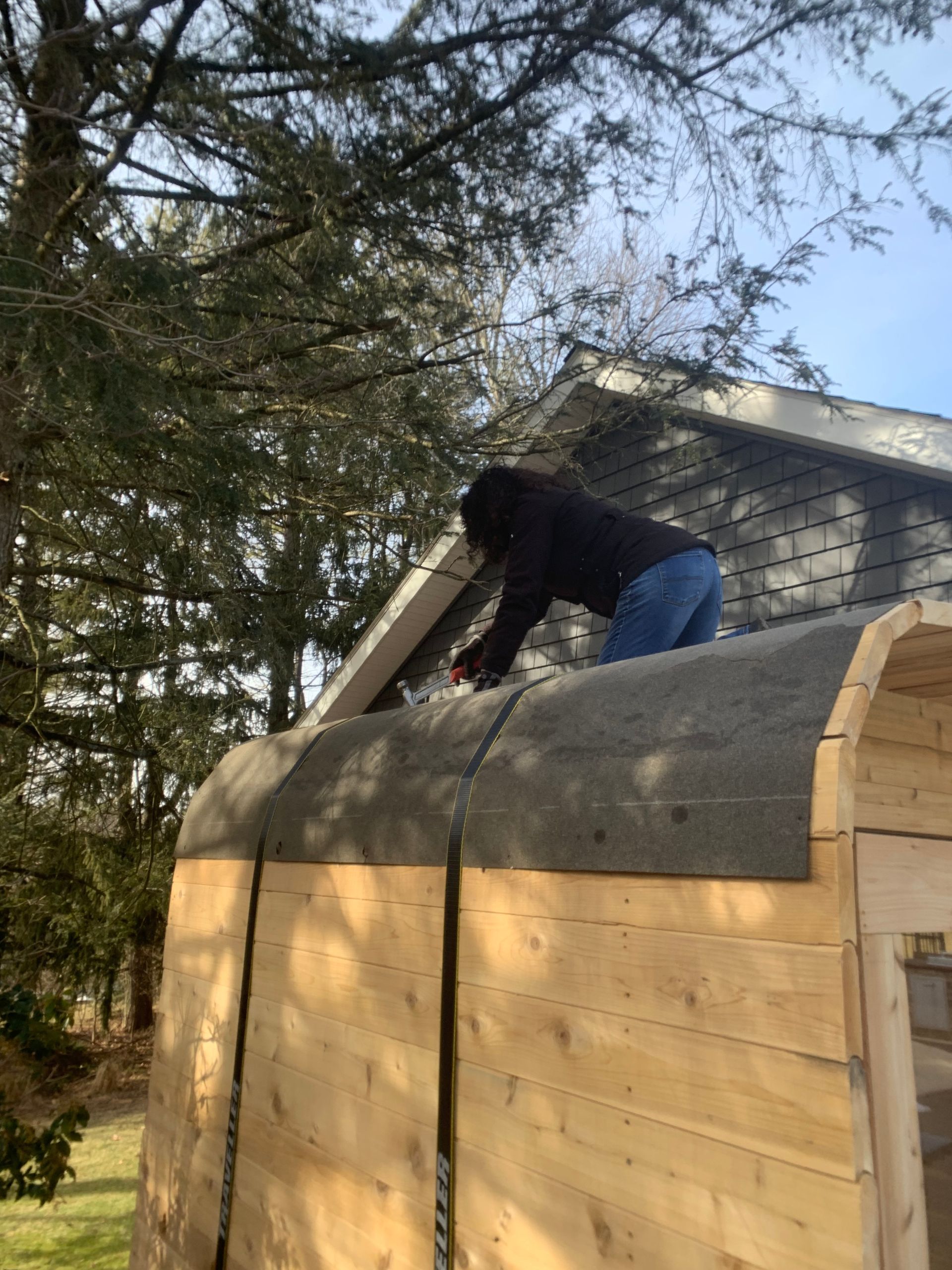 Person on a shed roof installing shingles on a wooden structure outdoors.