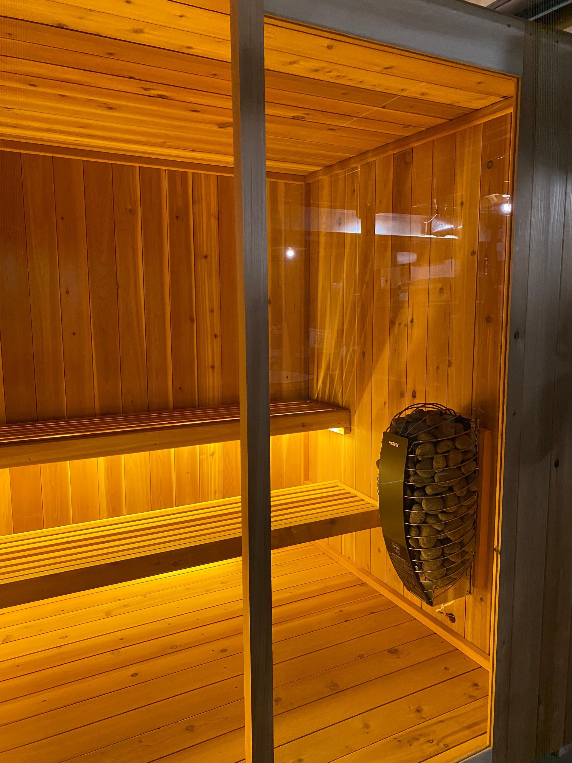 Wooden sauna interior with orange lighting, bench seating, and a stove or heater on the right