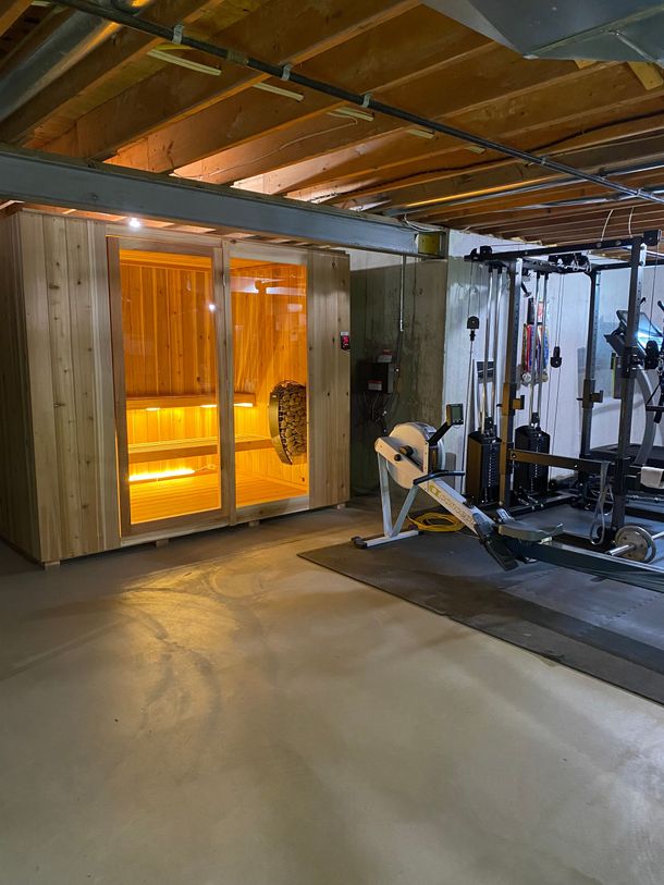 Home gym with wooden ceiling, glass doors, weight machine, and exercise equipment on a concrete floor.
