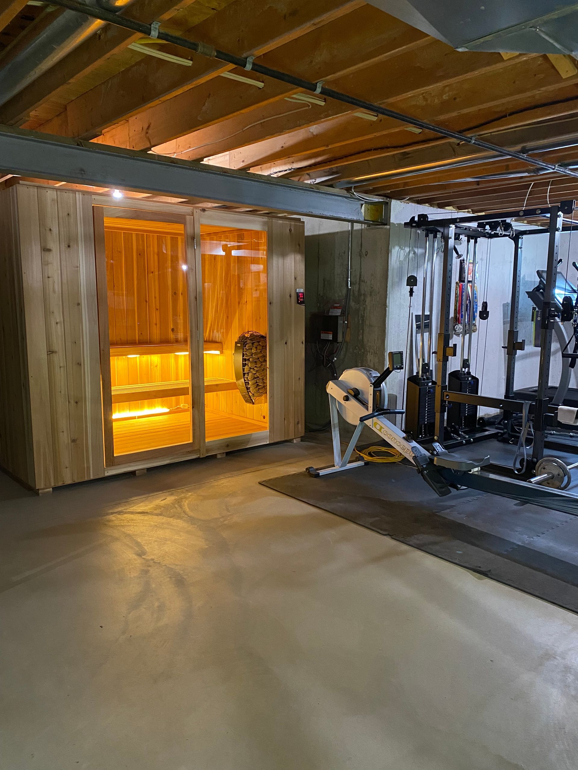 Home gym with weight machines, concrete floor, and orange-lit glass doors under a wood ceiling