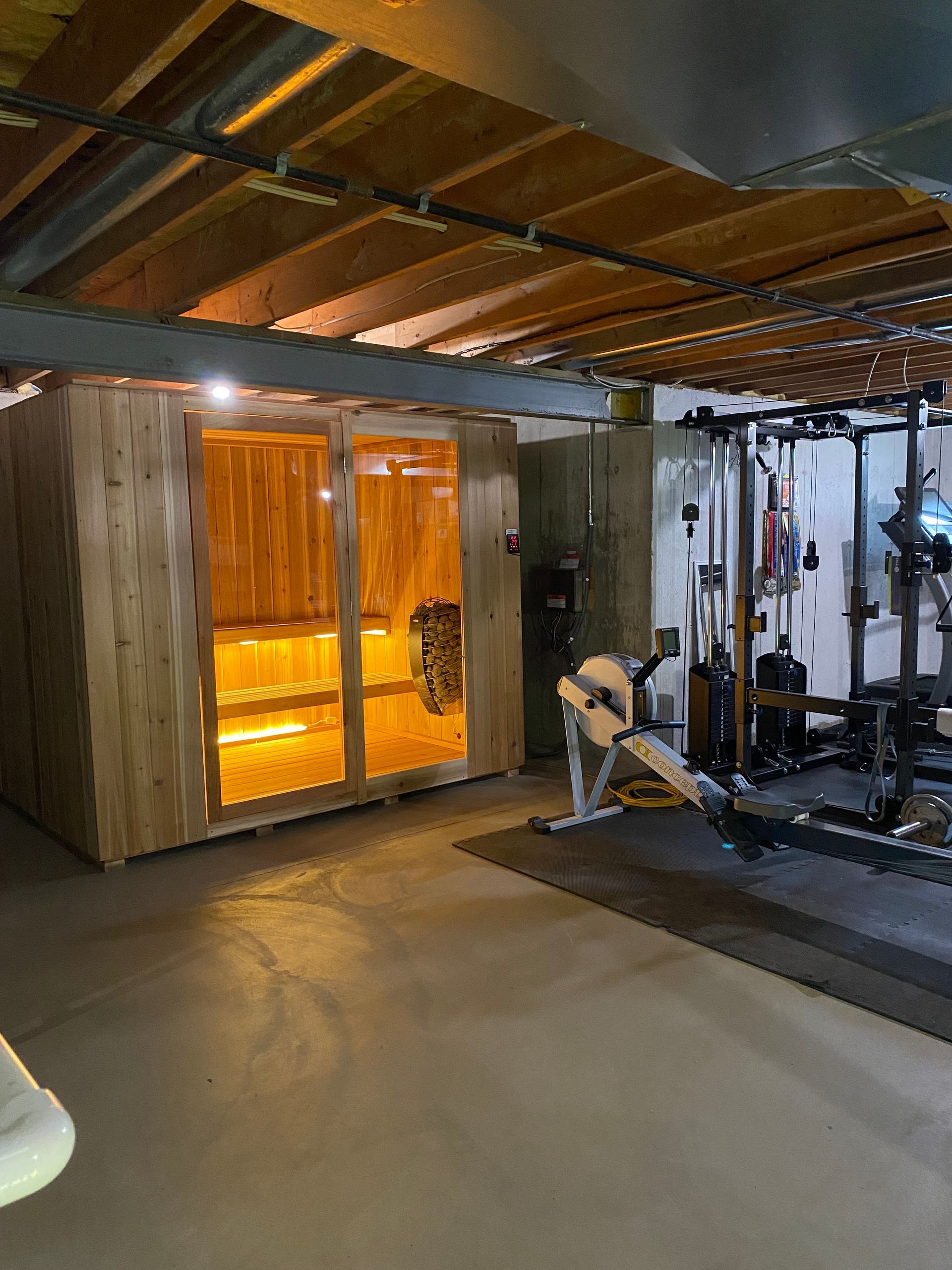 Basement home gym with tanning booth, weight rack, and exercise equipment under exposed ceiling beams