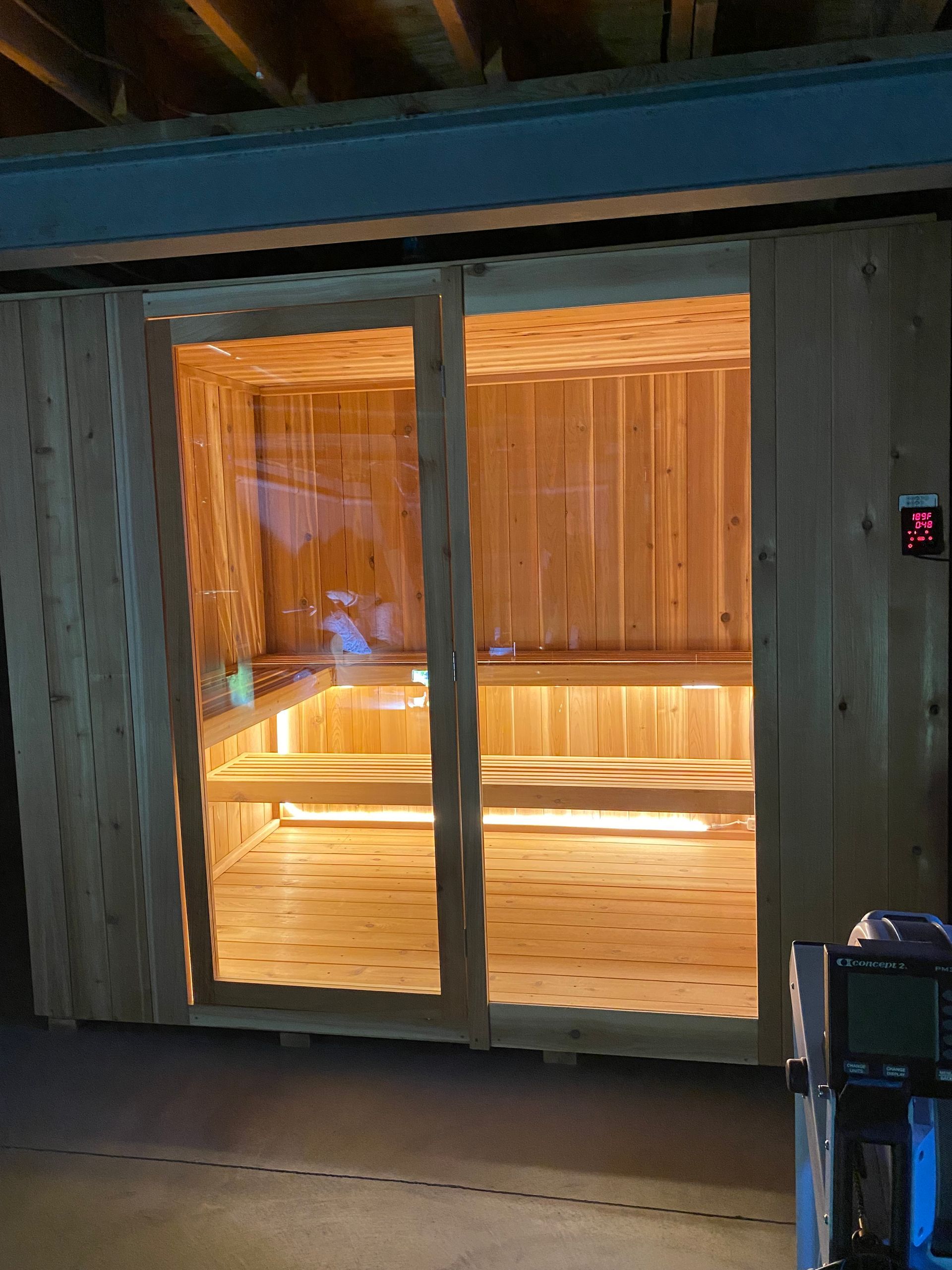 Wood-paneled sauna entrance with sliding glass doors glowing warm orange inside.