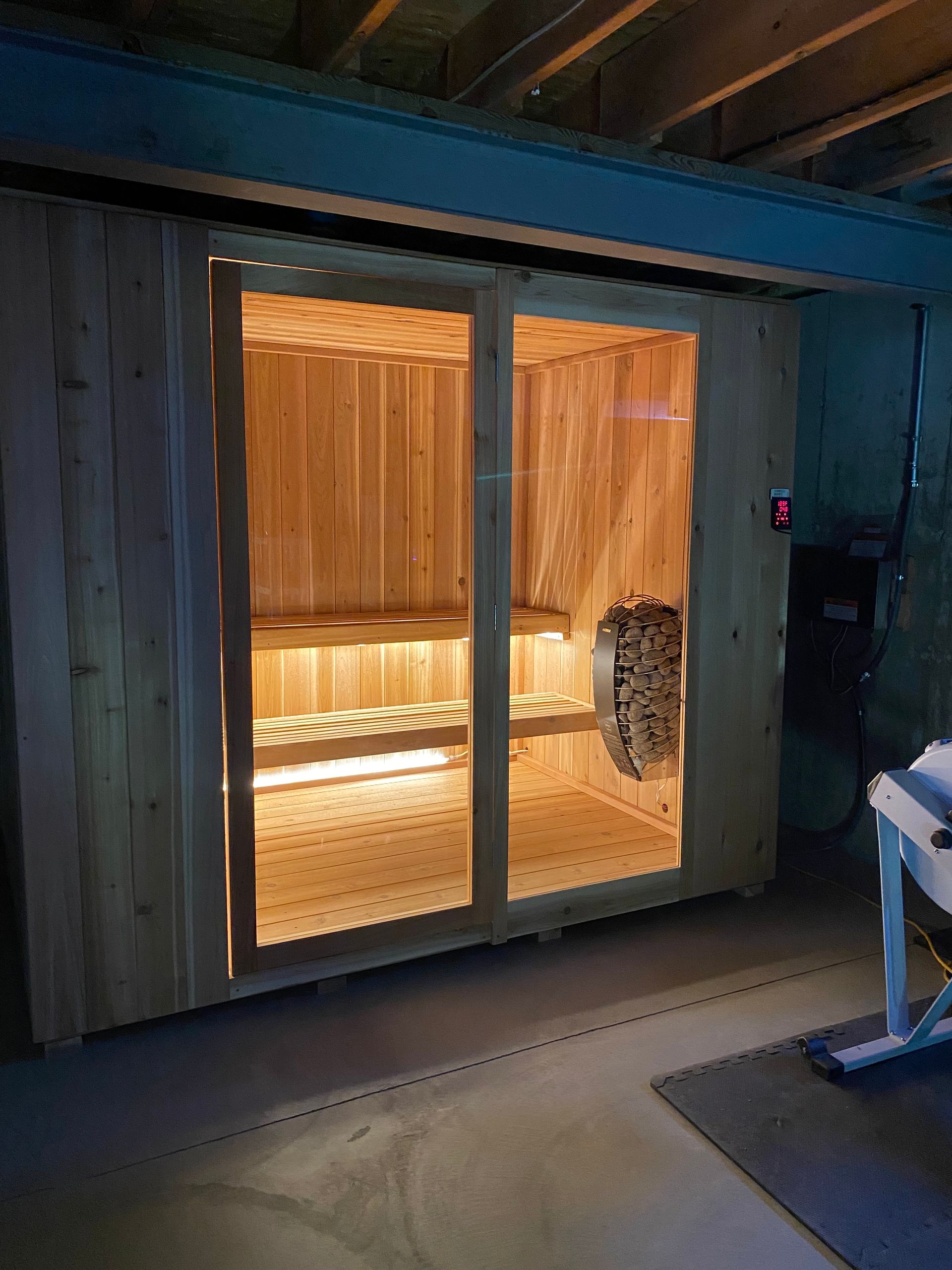 Wooden sauna interior behind sliding glass doors, softly lit in a dark room.