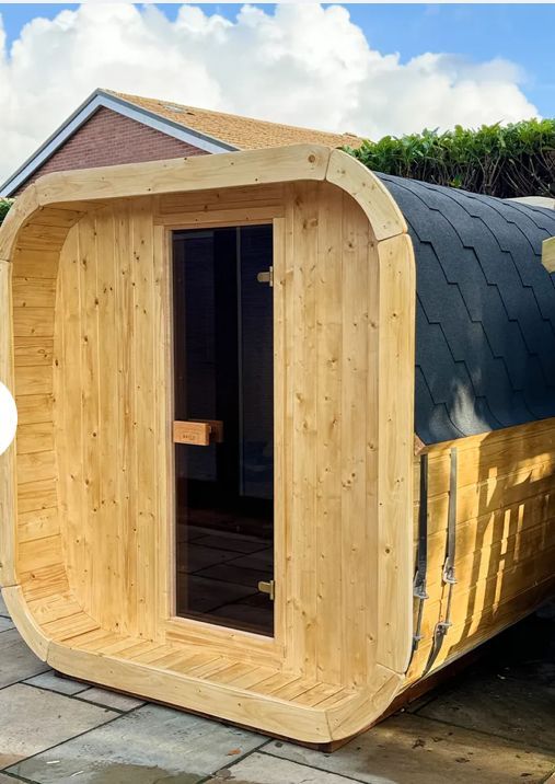 Wooden barrel sauna with curved black roof and open doorway outdoors in a backyard