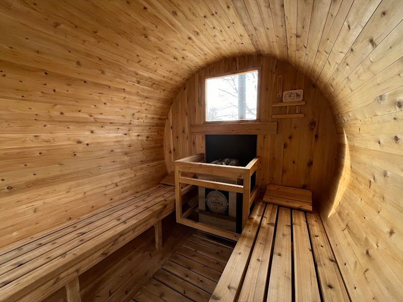 Wooden barrel sauna interior with bench seating, heater, and small window at the far end