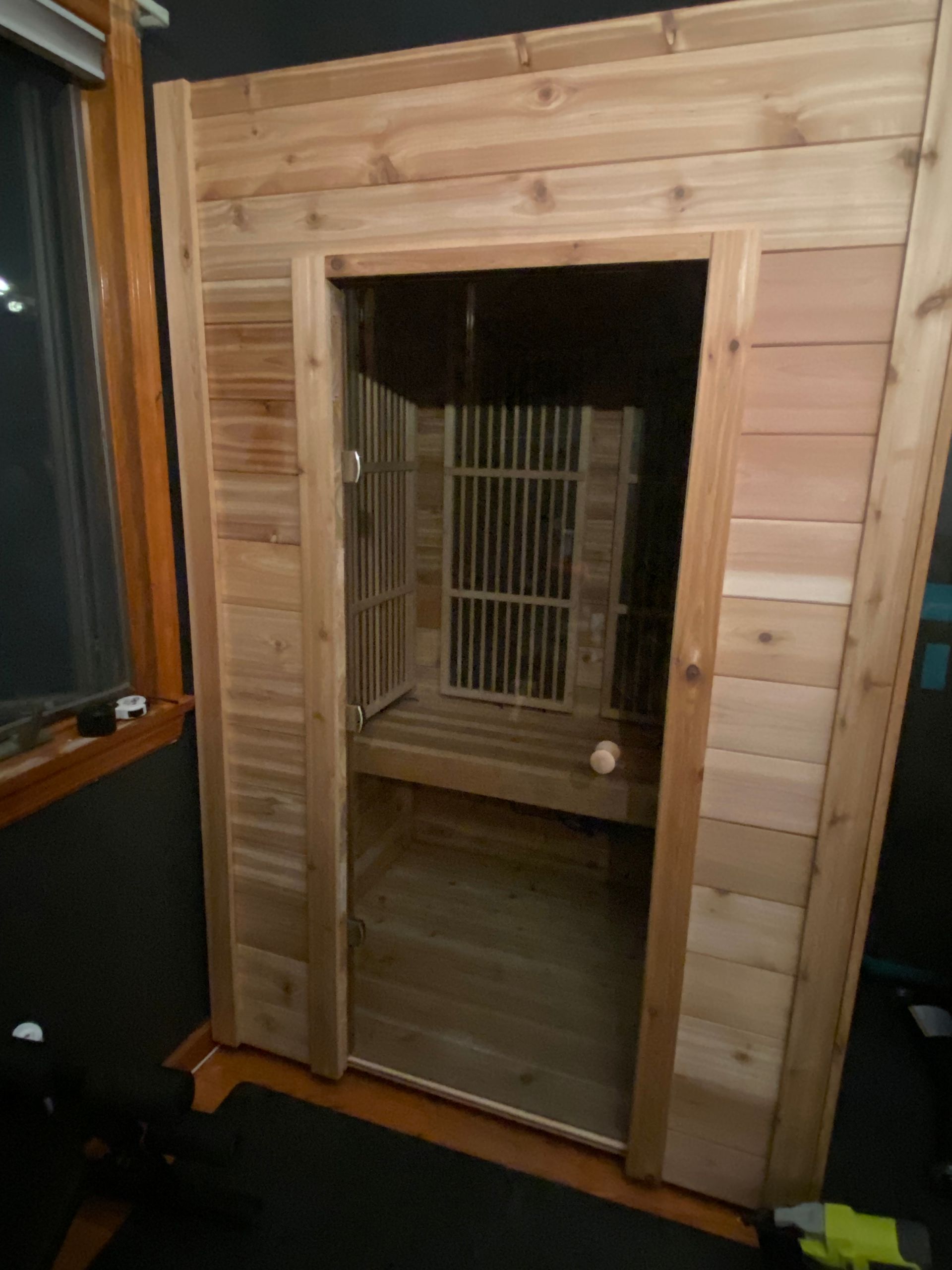 Wood-paneled indoor infrared sauna with a small doorway and gated enclosure inside.