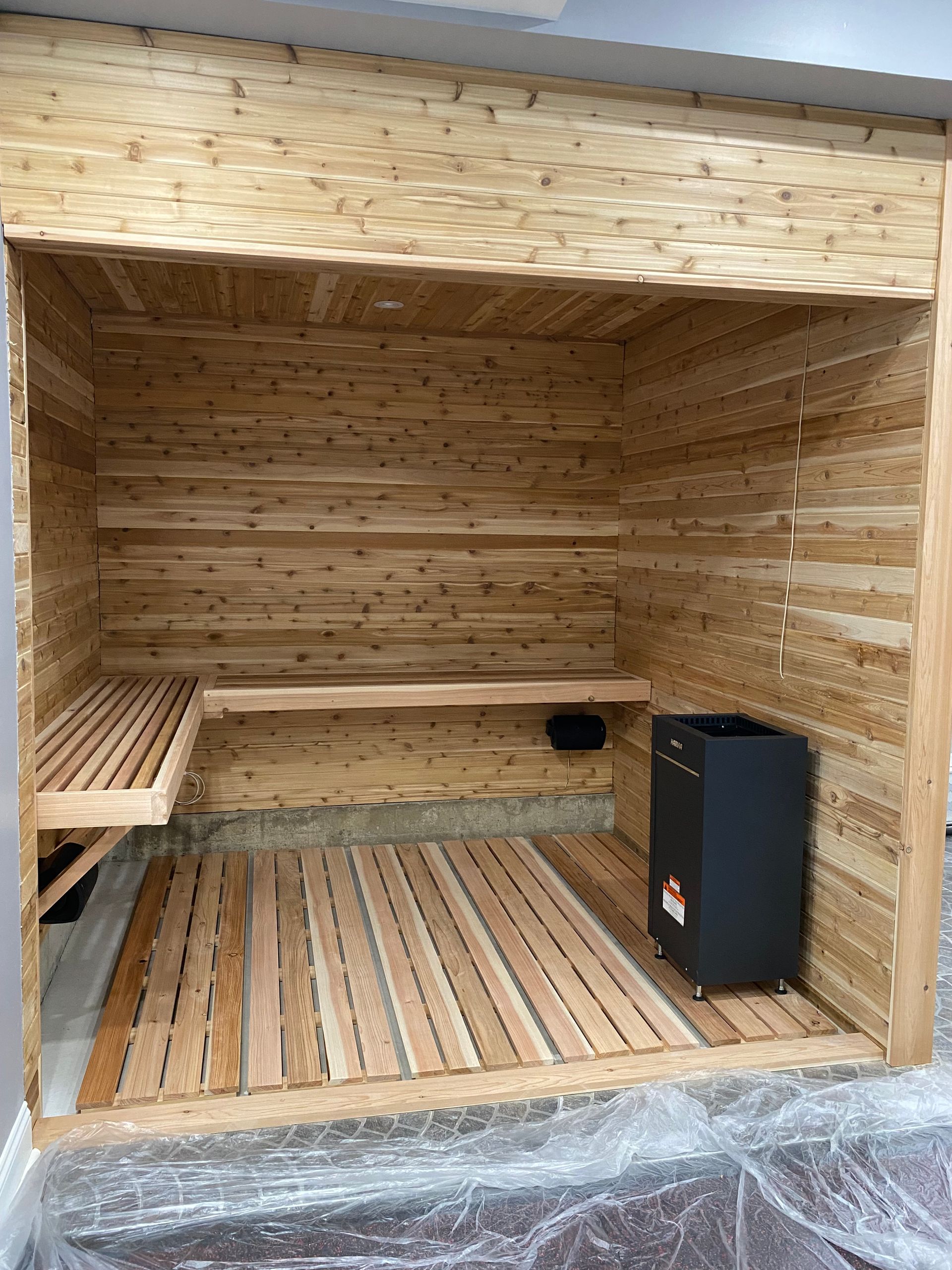 Wooden sauna interior with bench seating and a black heater on the right side