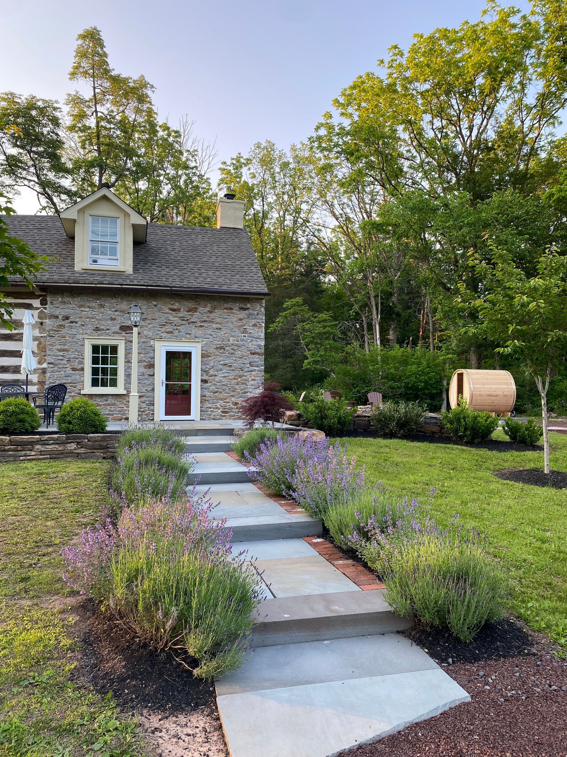 Stone cottage garden with a stepping-stone path, purple flowers, and trees in the background