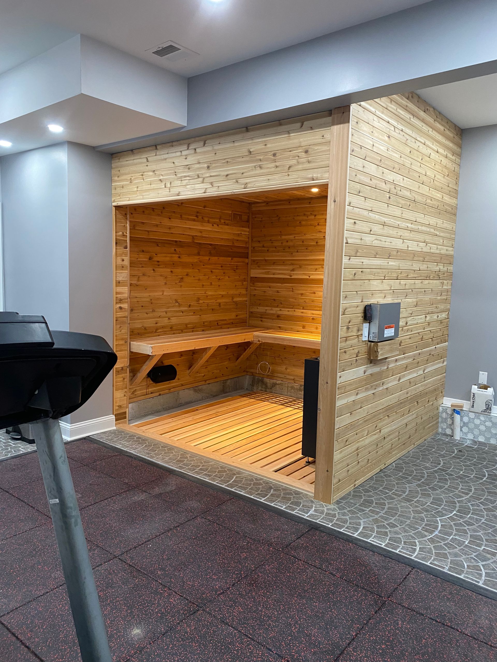 Wood-paneled indoor sauna with orange-lit bench and black reclining chair nearby