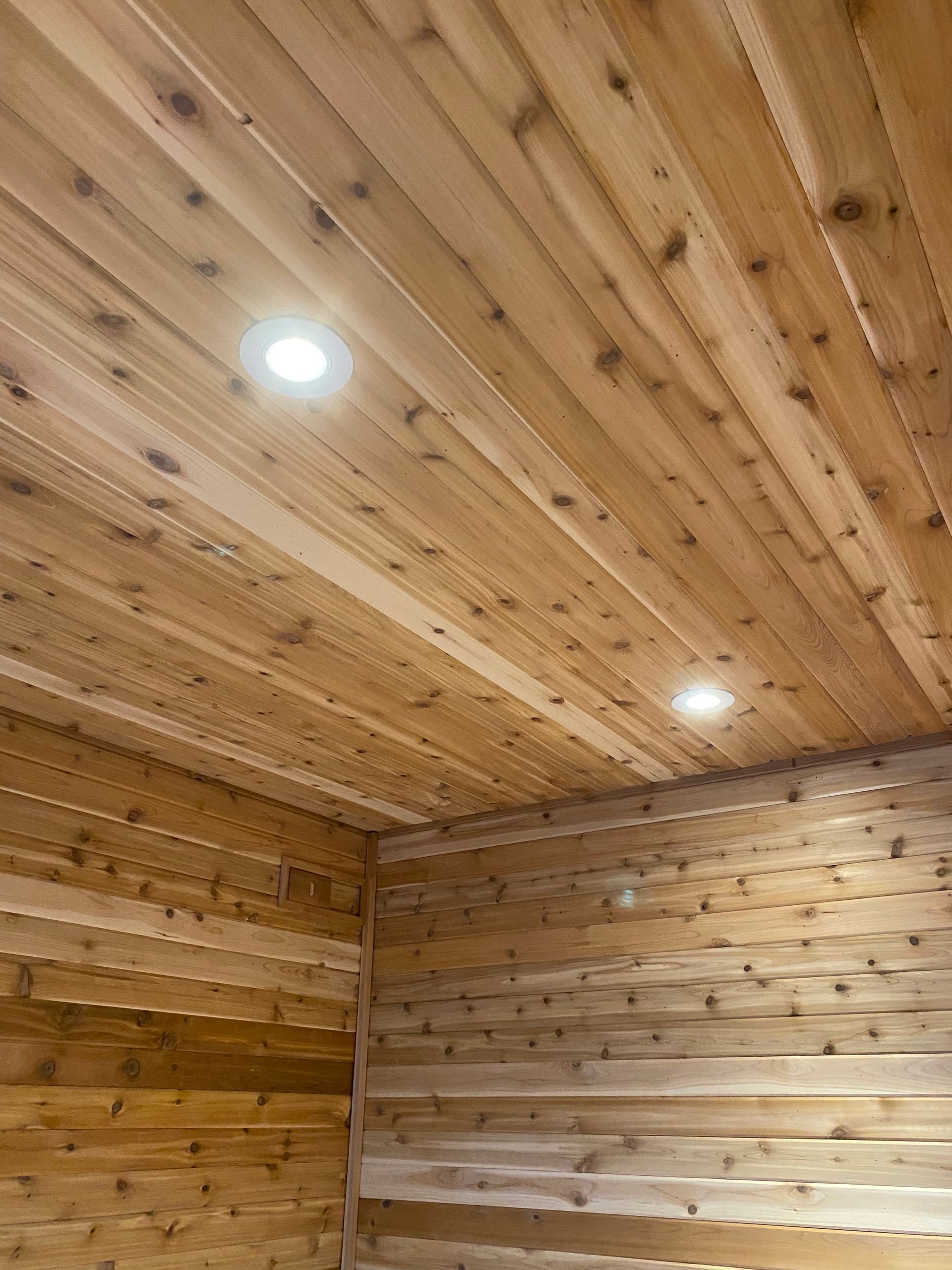 Wood-paneled sauna room with recessed ceiling lights and matching wooden walls.